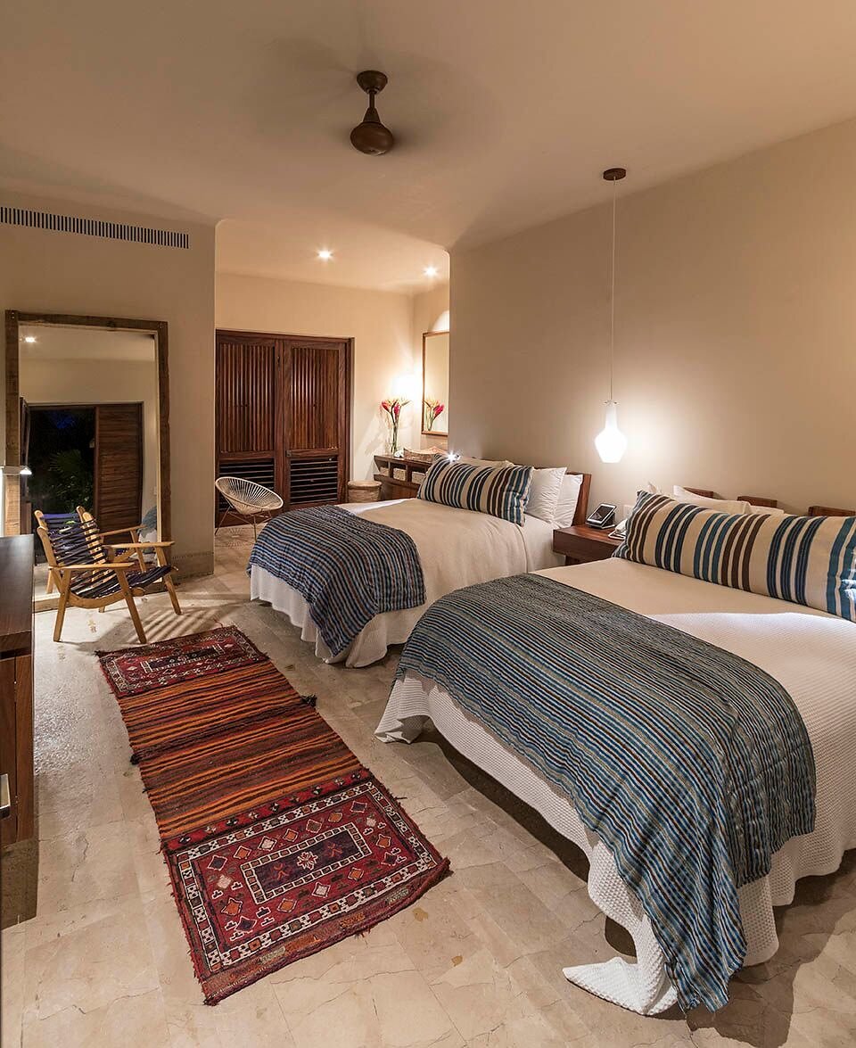 Two queen beds with blue-striped throws and a woven runner between them, louvered wood closet doors, a terrace with an Acapulco chair visible through open sliding panels, Casa Escondida, Ranchos Estates, Punta Mita.