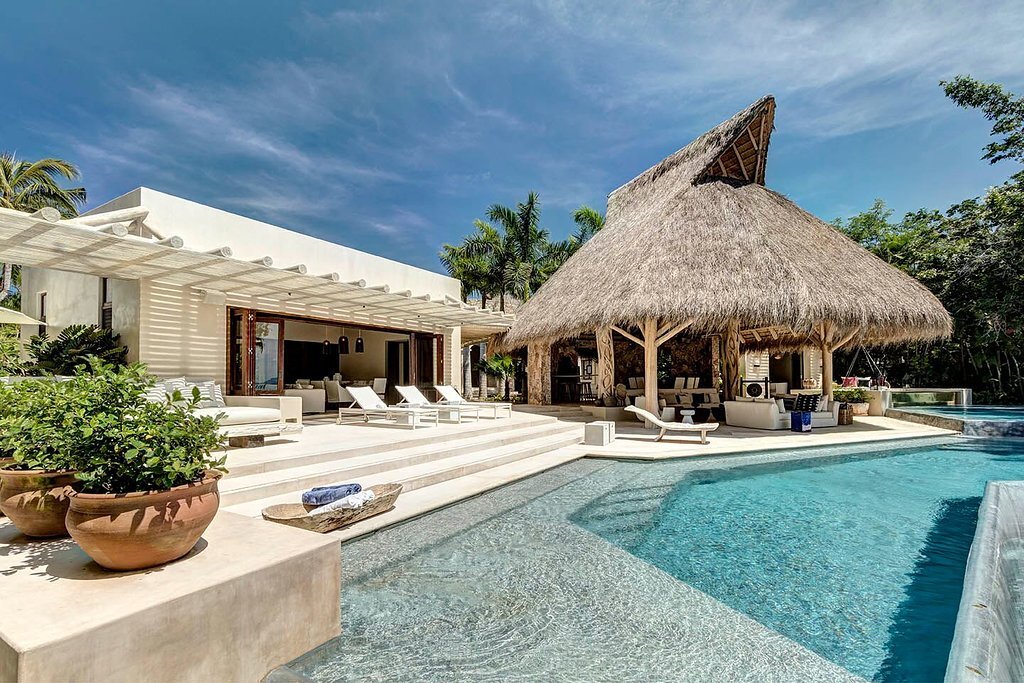 Pool deck with terracotta planters, cushioned lounge chairs, a large open palapa bar and lounge, and the villa's open living pavilion with a mounted television visible in the background, Casa Escondida, Ranchos Estates, Punta Mita.
