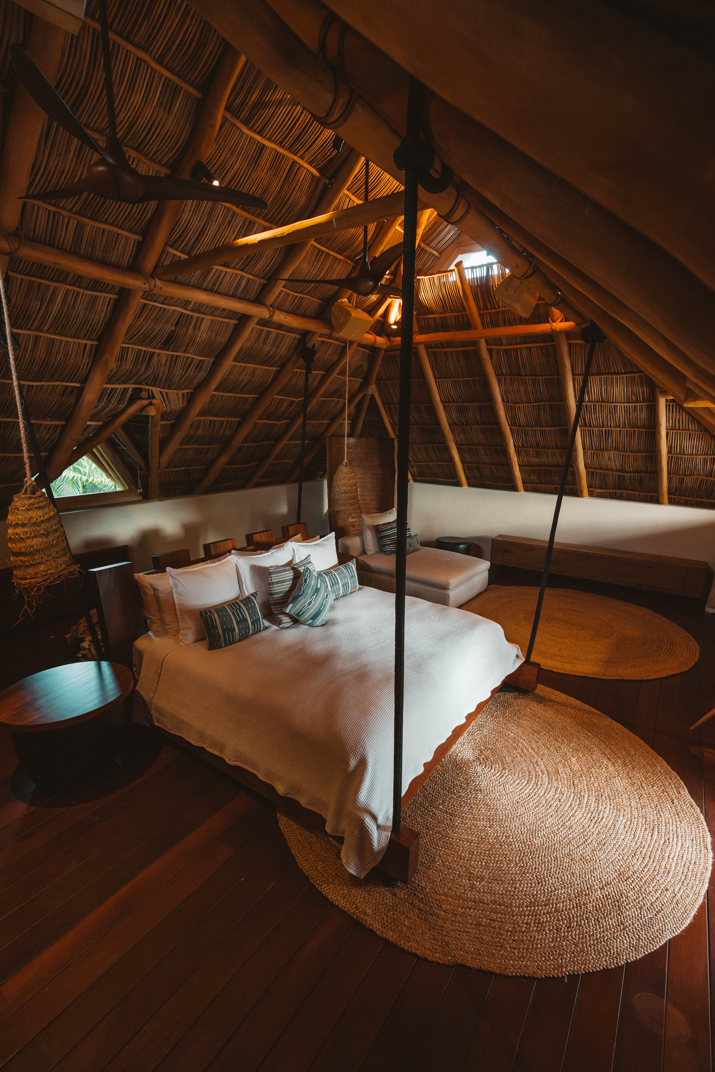 Palapa suite with exposed bamboo ceiling rafters, a rope-hung four-poster bed with striped pillows, dark hardwood floors, and an oval jute rug, Casa Escondida, Ranchos Estates, Punta Mita.