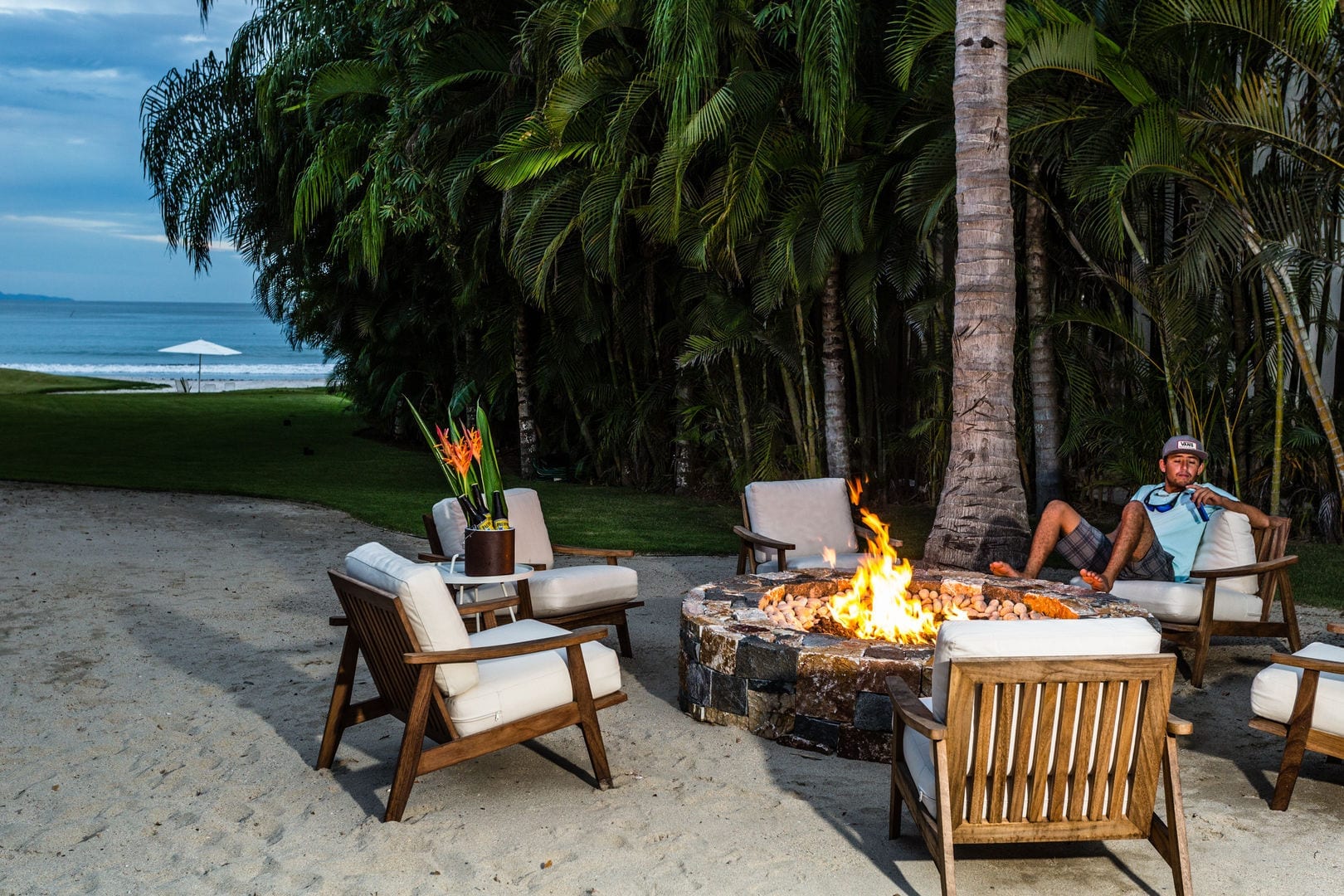 Stone fire pit on beachfront sand with teak lounge chairs, royal palms, and the Pacific surf at dusk, Casa Escondida, Ranchos Estates, Punta Mita.