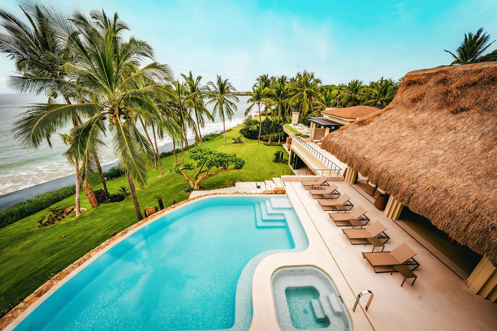 Elevated view from above the palapa showing the crescent pool and spa below, a row of sun loungers on the pool deck, beachfront lawn and Pacific Ocean stretching to the horizon, Casa Happy Paws, Ranchos Estates, Punta Mita.