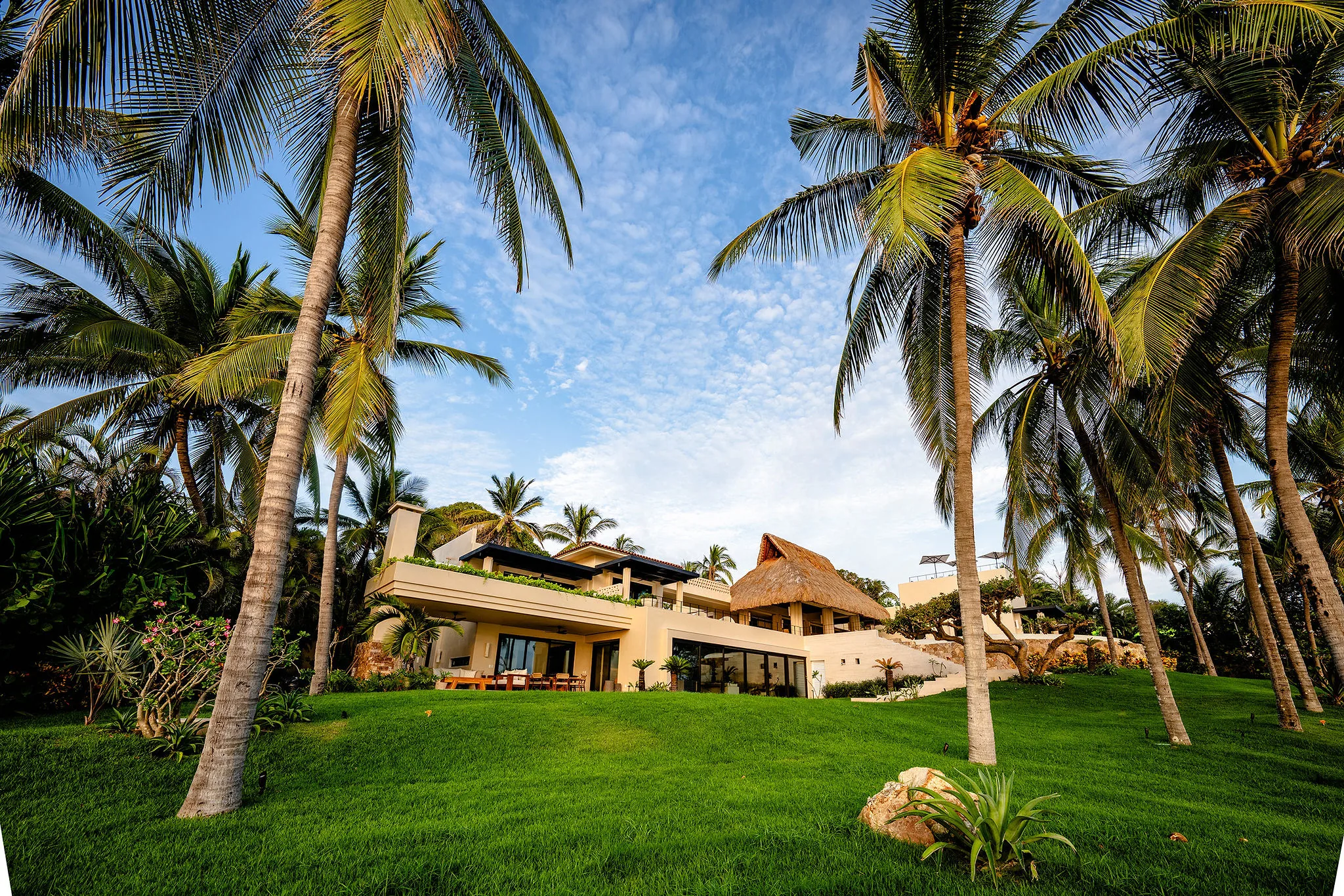 Coconut palms frame the two-story white villa and thatched palapa at mid-morning, Casa Happy Paws, Ranchos Estates, Punta Mita.