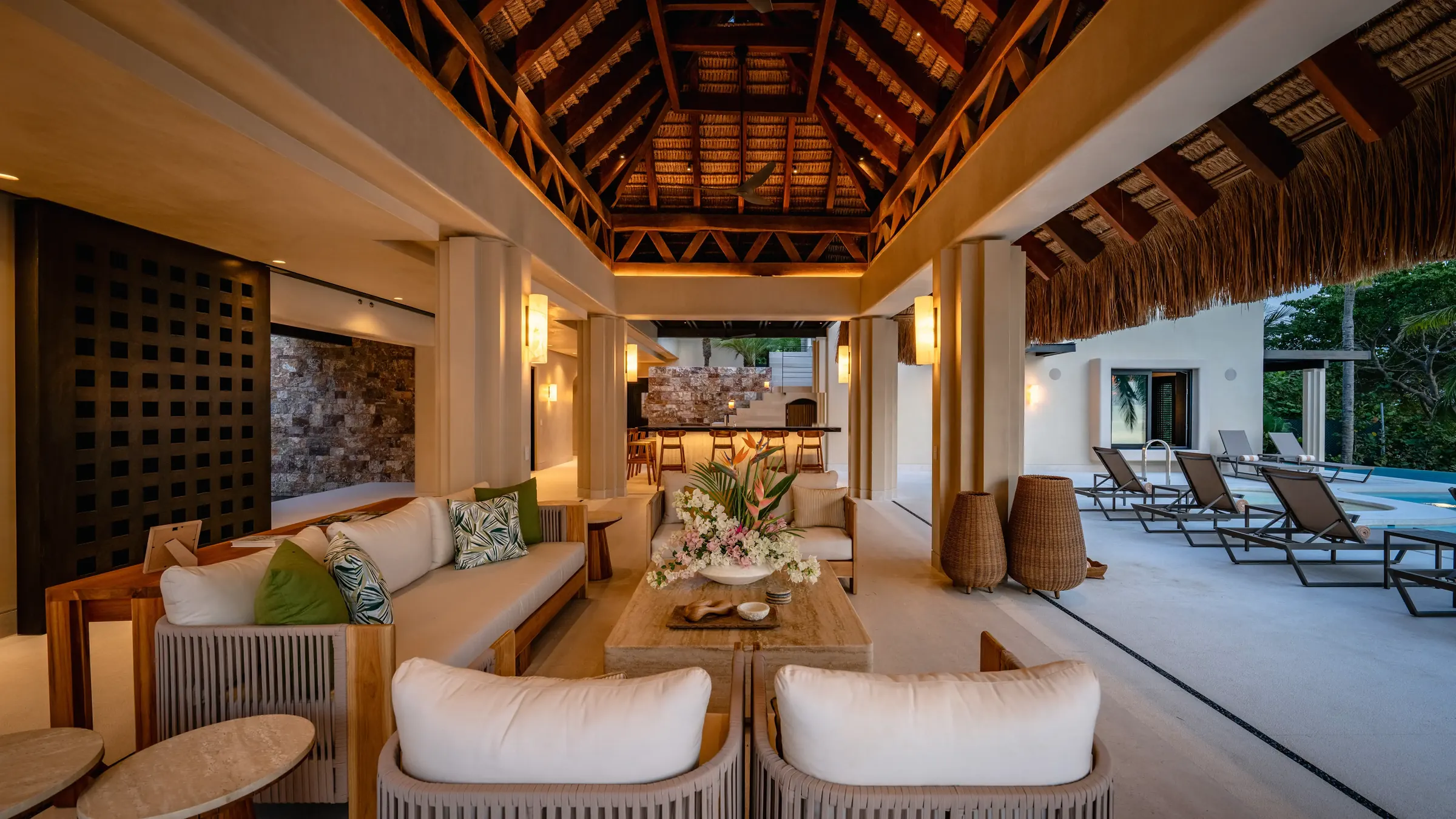Open-air living pavilion with exposed beam palapa ceiling, white sofas and tropical cushions, bar visible in the background and pool loungers to the right, Casa Happy Paws, Ranchos Estates, Punta Mita.