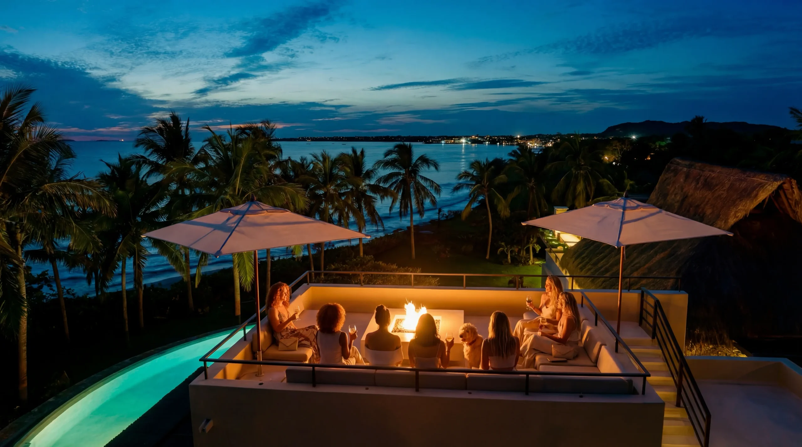 Guests gather at the sunken rooftop fire-pit lounge at dusk, parasols framing a wide-angle view of palms and the Pacific bay beyond, Casa Happy Paws, Ranchos Estates, Punta Mita.