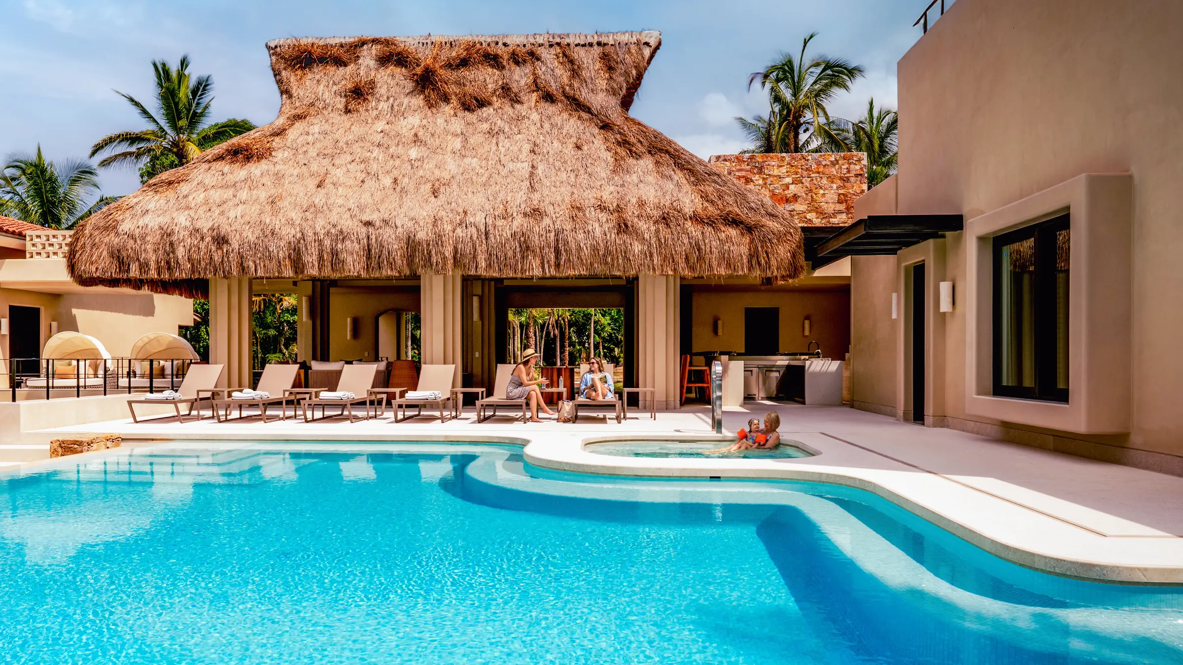 Curved kidney pool with white coping reflecting the thatched palapa pavilion and white villa facade, sun loungers arranged poolside, Casa Happy Paws, Ranchos Estates, Punta Mita.