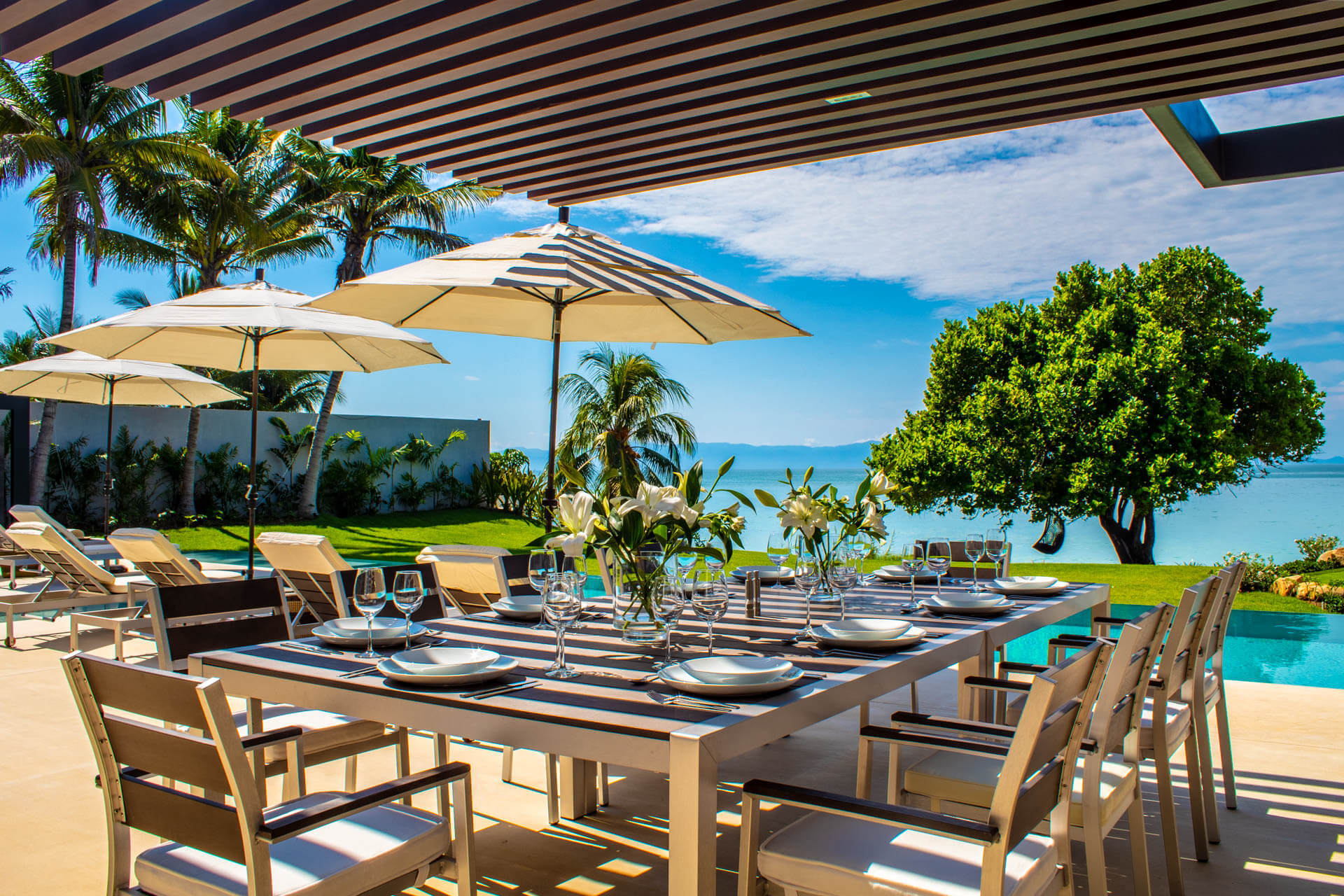 Ten-seat outdoor dining table set with glassware and white umbrellas, ocean beyond, Estate Afrique, Ranchos Estates, Punta Mita.