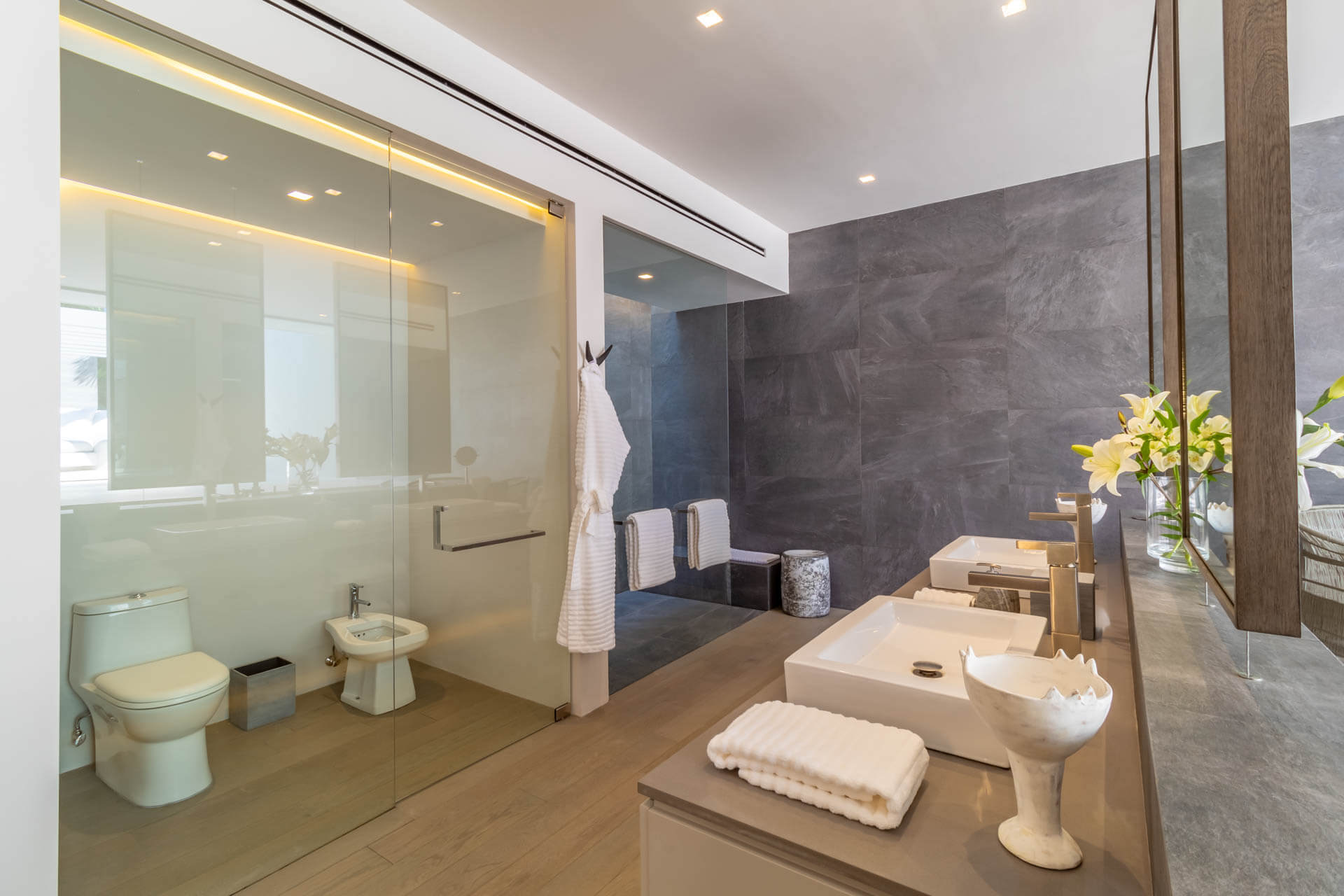 Guest ensuite bath with glass-enclosed WC, dark slate accent wall, and double vessel-sink vanity, Estate Afrique, Ranchos Estates, Punta Mita.