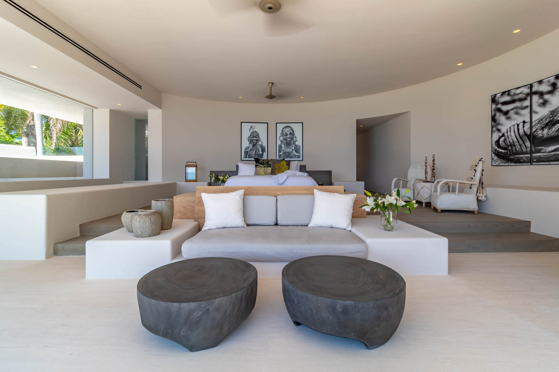 Primary suite wide view with curved ceiling, pair of African portrait photographs, stone coffee tables, and garden access, Estate Afrique, Ranchos Estates, Punta Mita.