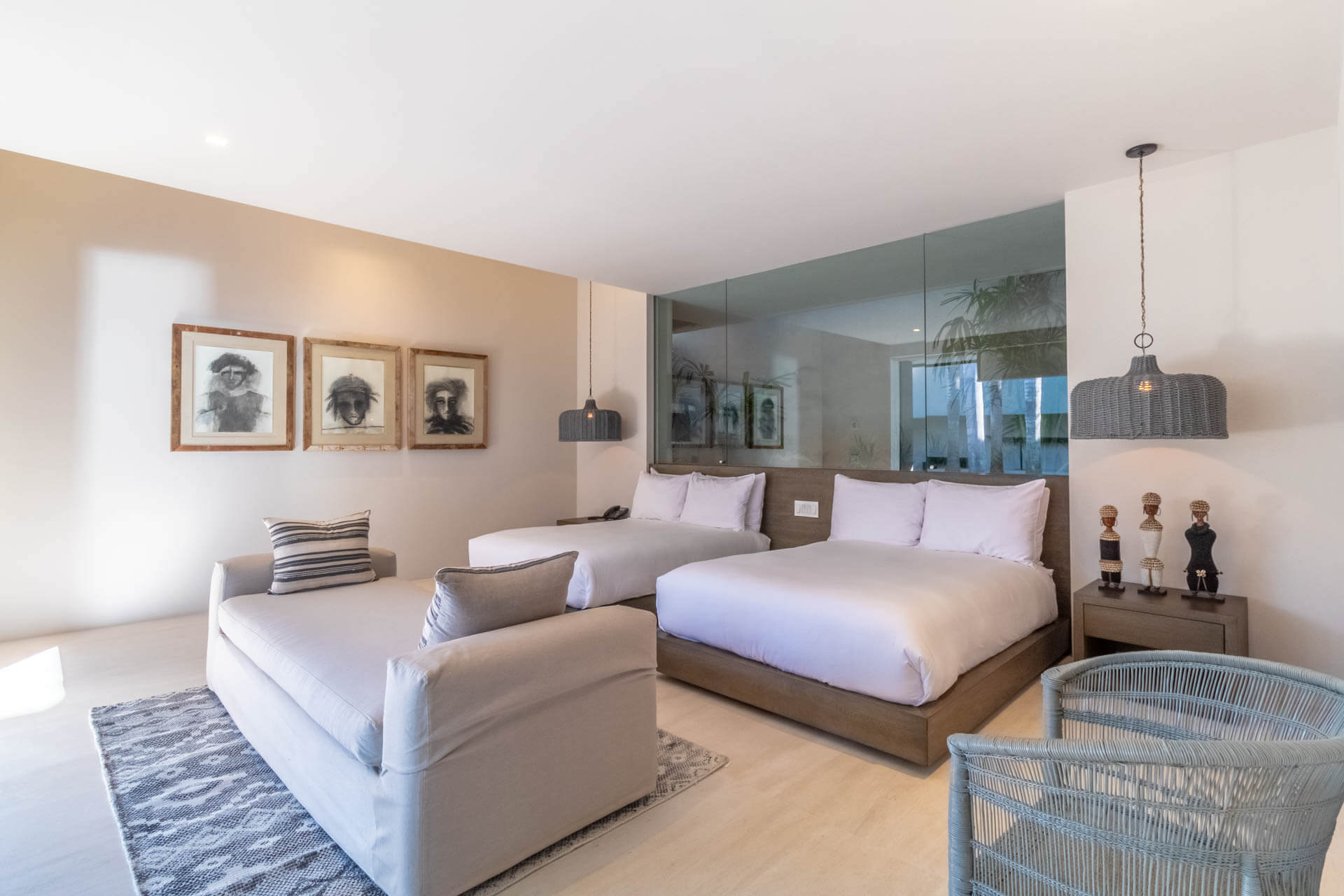 Guest suite with two double beds, three African charcoal portraits, glass-partition bathroom, and rattan pendant lights, Estate Afrique, Ranchos Estates, Punta Mita.