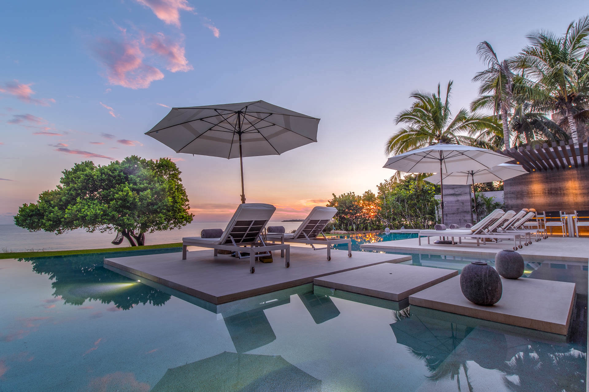 Infinity pool at dusk with raised sun-deck island, lounge chairs, umbrellas, and pink-streaked sky over the ocean, Estate Afrique, Ranchos Estates, Punta Mita.