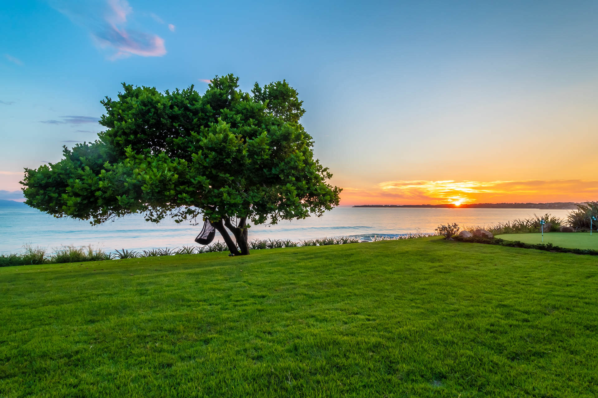 Beachfront lawn at sunset with signature broad mango tree, hammock chair, and Banderas Bay horizon, Estate Afrique, Ranchos Estates, Punta Mita.