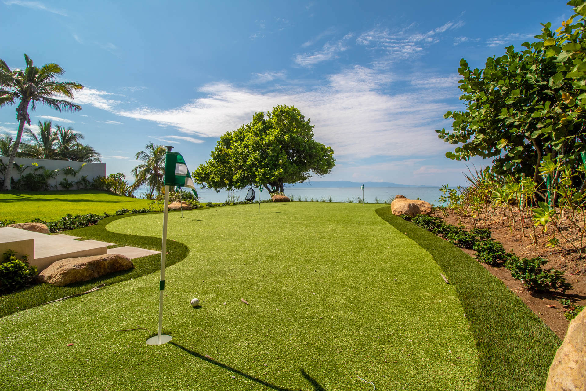 Private putting green with flag, sculptured landscape boulders, and Pacific ocean and mango tree in the background, Estate Afrique, Ranchos Estates, Punta Mita.