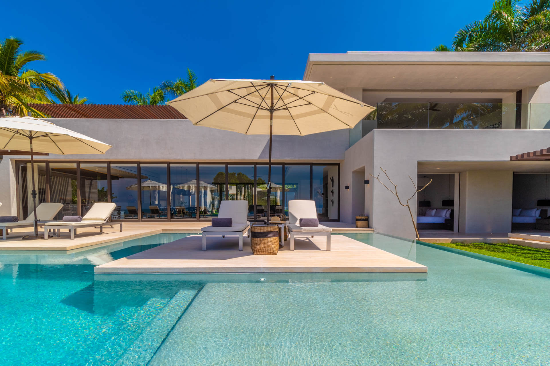 Pool with mid-water sun-deck island, two lounge chairs, and umbrella backed by white stucco villa facade, Estate Afrique, Ranchos Estates, Punta Mita.
