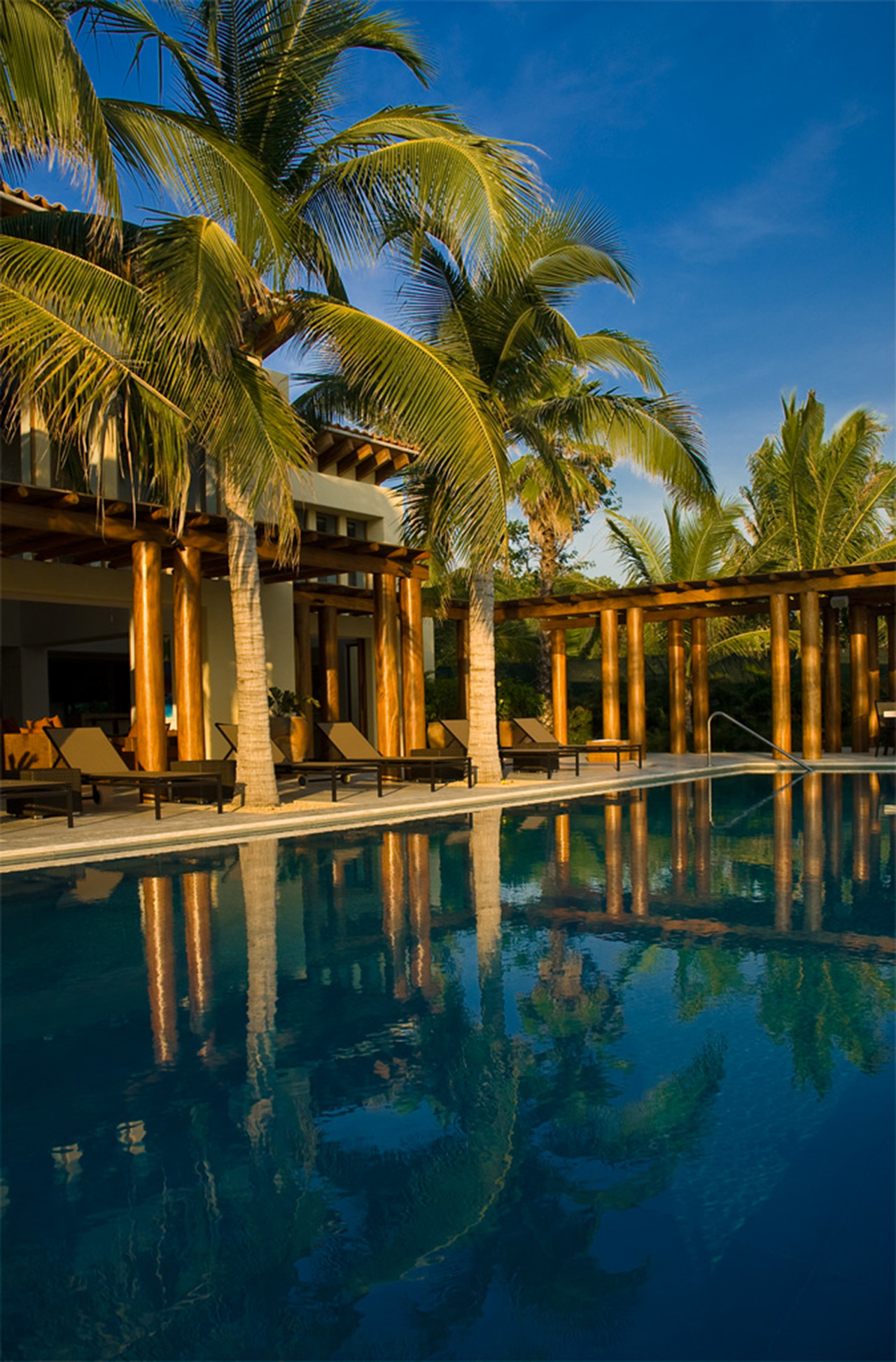 Palm-column colonnade and pool deck lit by late-afternoon sun, Estate Jaguar, Ranchos Estates, Punta Mita.