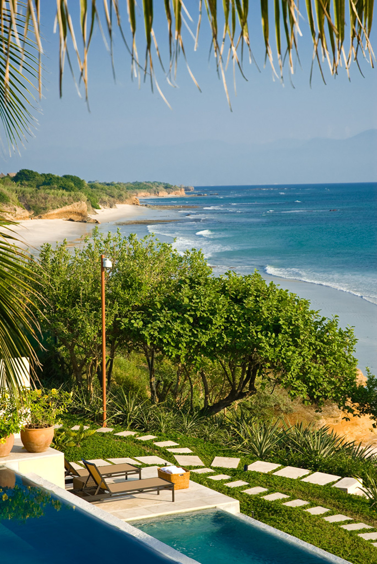Pool-edge loungers on a stepping-stone path descending through tropical garden to the Punta Mita coastline and red sandstone cliffs, Estate Jaguar, Ranchos Estates, Punta Mita.