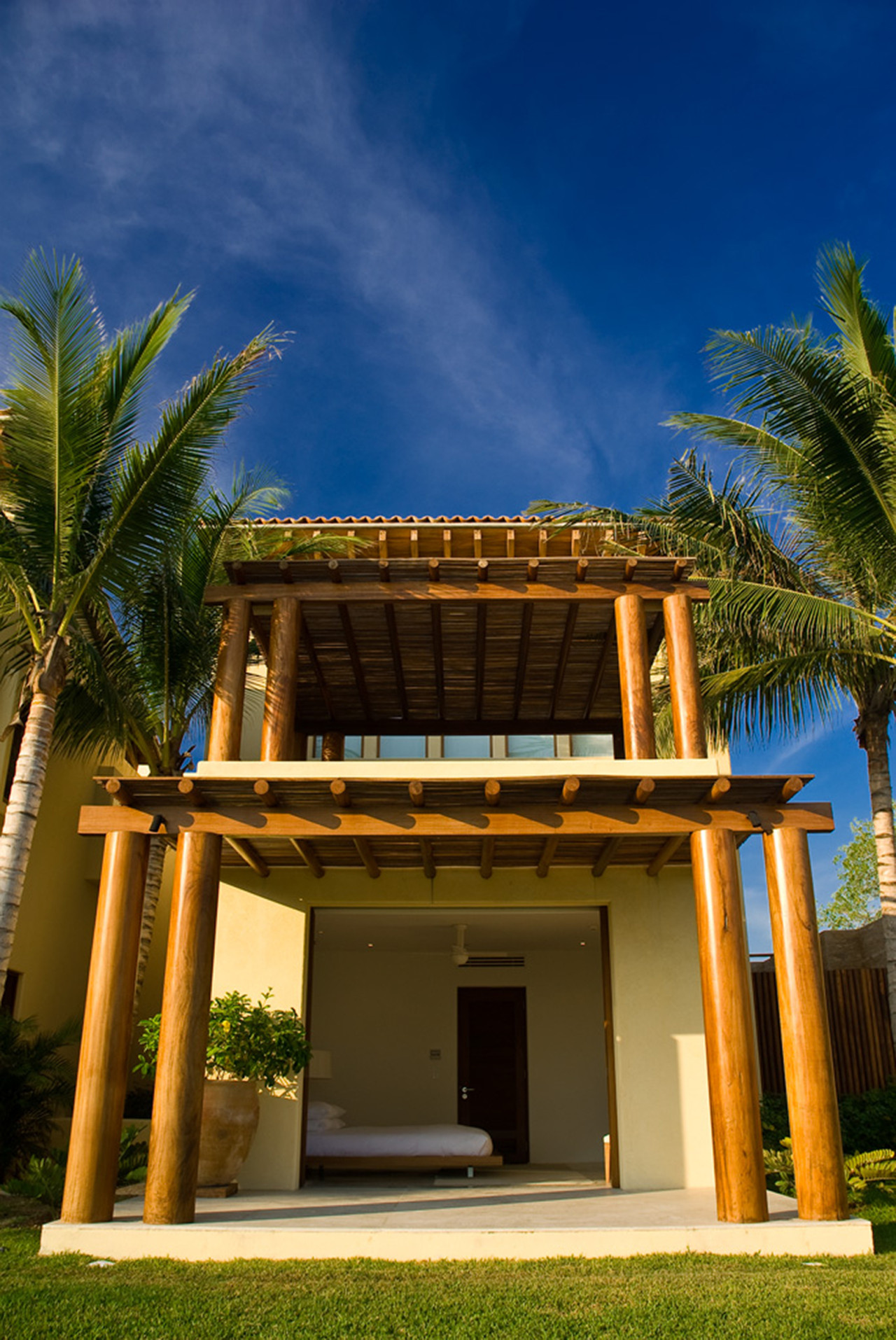 Open-air guest suite bungalow with double wood-column palapa canopy and bed visible inside cream stucco walls, Estate Jaguar, Ranchos Estates, Punta Mita.
