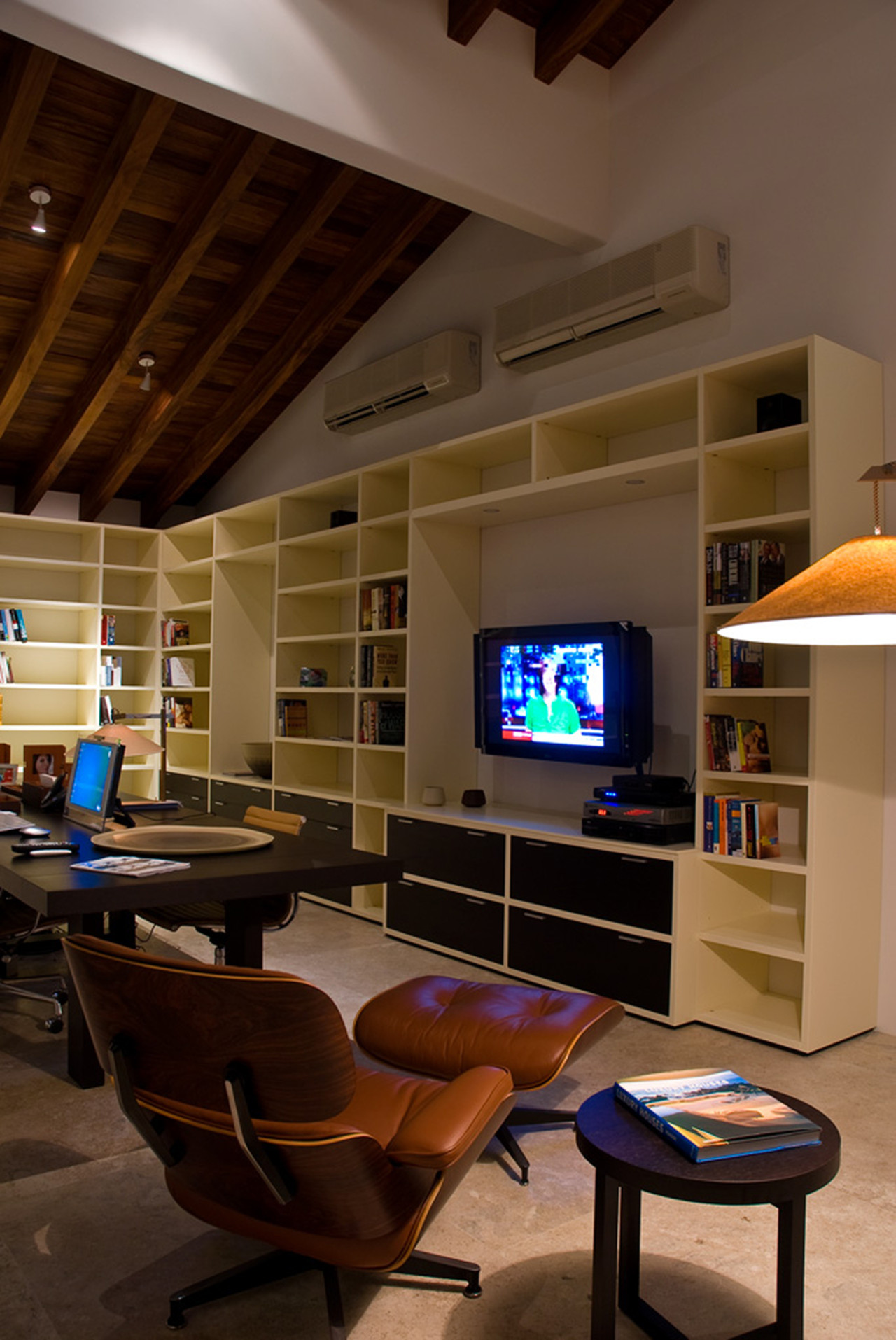 Media room with exposed dark-beam cathedral ceiling, floor-to-ceiling built-in shelving, flat-screen TV, and Eames lounge chair, Estate Jaguar, Ranchos Estates, Punta Mita.