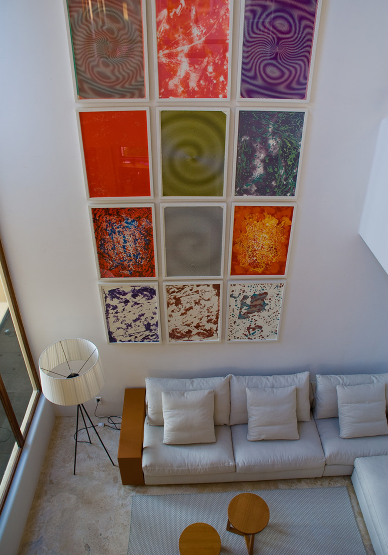 Double-height living pavilion viewed from an upper landing, showing a twelve-panel grid of abstract prints above a low white sectional, Estate Jaguar, Ranchos Estates, Punta Mita.