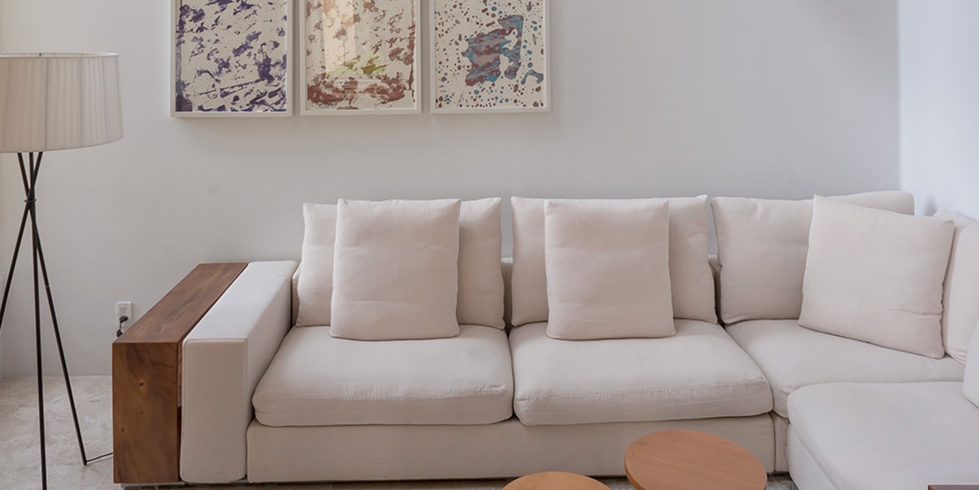Living area with a low cream sectional sofa, three abstract prints above, and a walnut side console, Estate Jaguar, Ranchos Estates, Punta Mita.