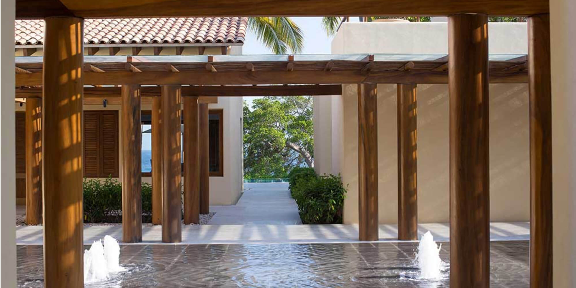 Formal entry pergola with wood columns over a reflecting pool with two fountain jets, ocean visible at the far end of the passageway, Estate Jaguar, Ranchos Estates, Punta Mita.