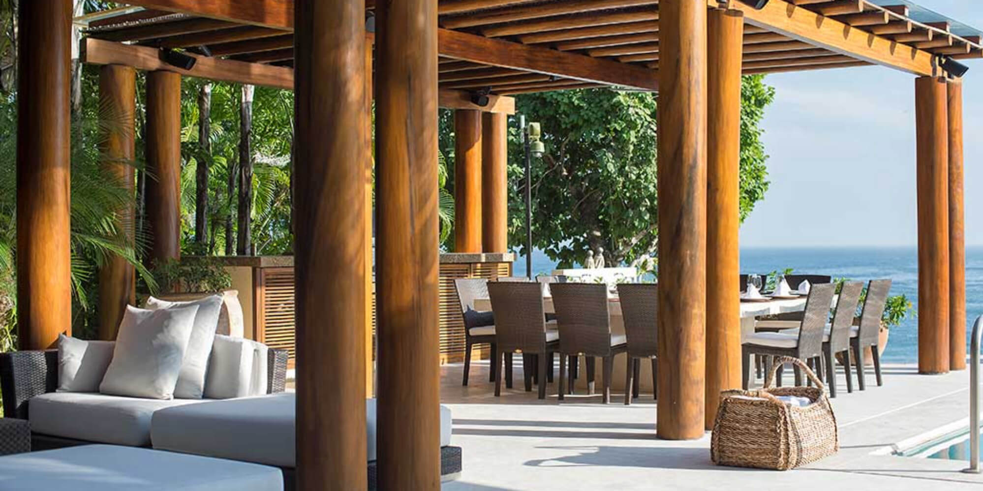 Outdoor dining table set for ten under a wood pergola, with lounge seating beside it and the Pacific Ocean visible beyond, Estate Jaguar, Ranchos Estates, Punta Mita.