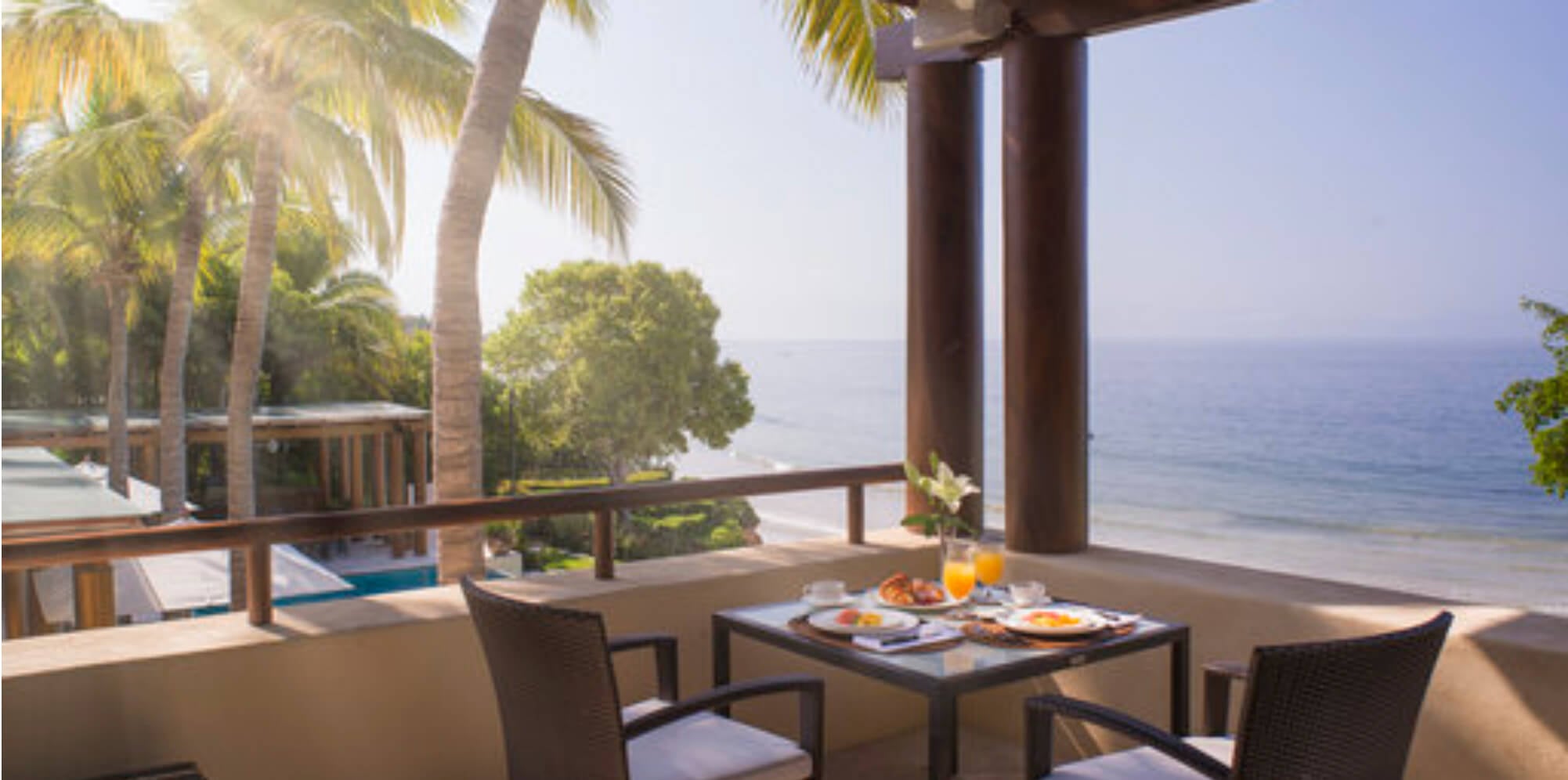 Private balcony with a breakfast table set for two, rattan chairs, a wood pergola overhead, and the beach and Pacific below in morning light, Estate Jaguar, Ranchos Estates, Punta Mita.