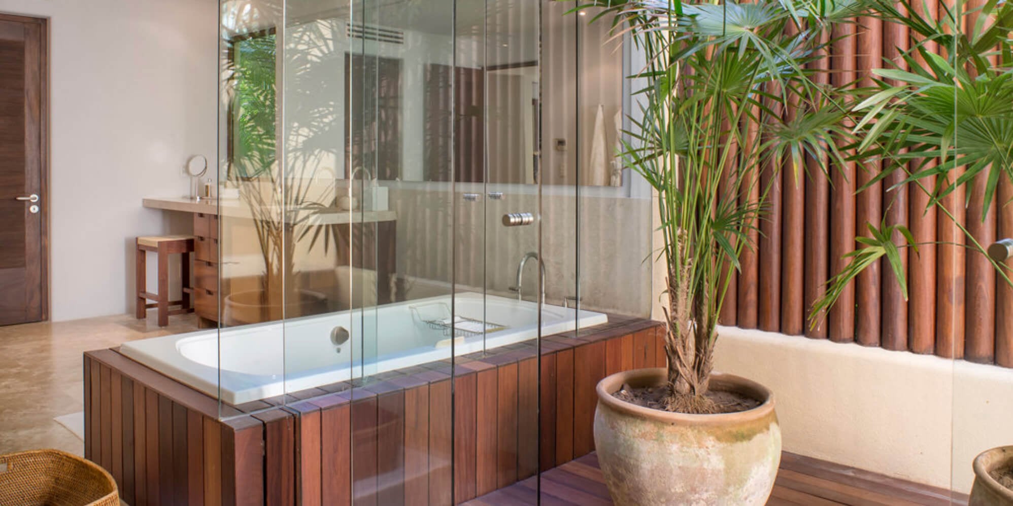 Glass-walled soaking tub with a dark wood surround beside a potted palm and a vertical wood-slat privacy screen, Estate Jaguar, Ranchos Estates, Punta Mita.