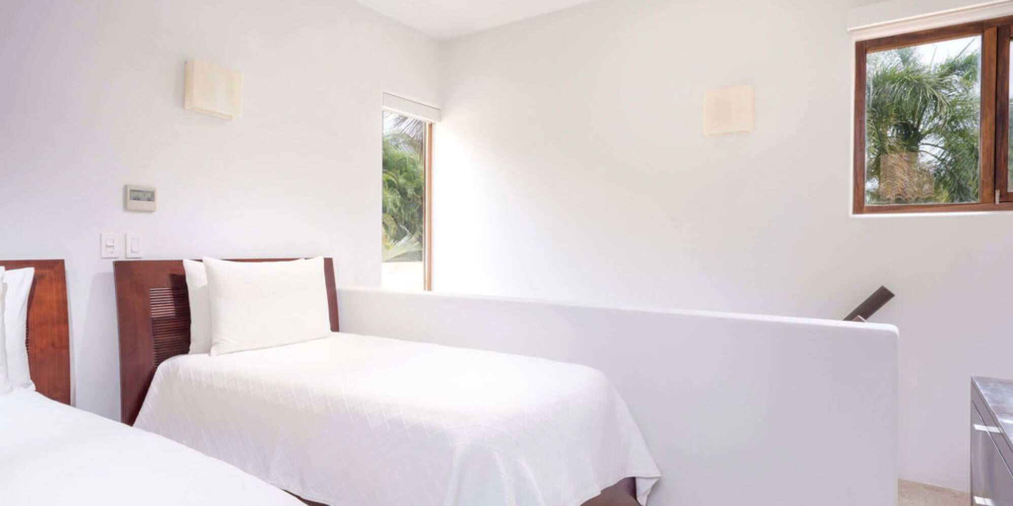 Twin-bed guest room with dark wood slatted headboards, crisp white linens, and wood-framed windows looking out to palms, Estate Jaguar, Ranchos Estates, Punta Mita.