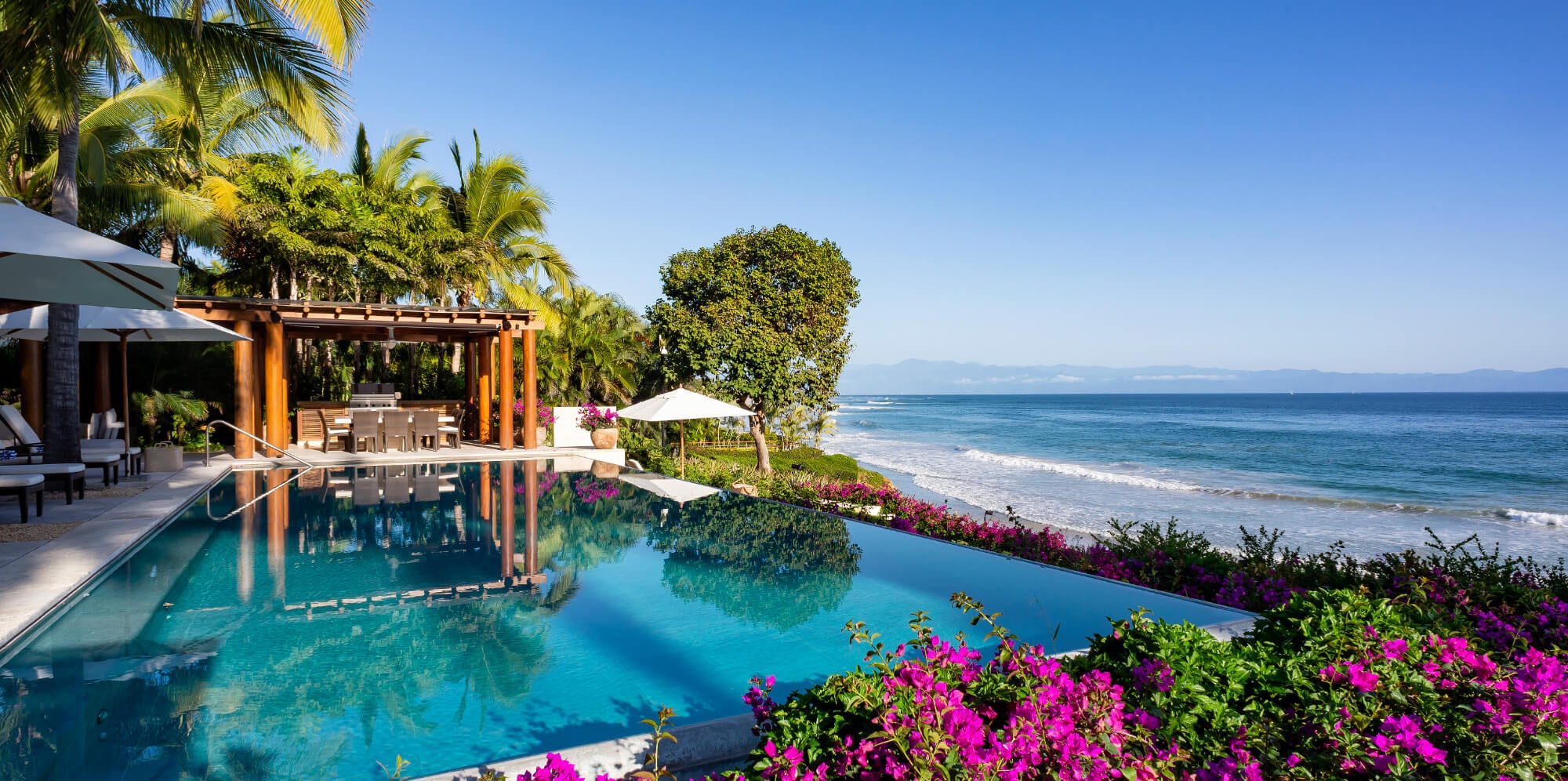 Infinity pool bordered by bougainvillea with a wood pergola pavilion, beach umbrellas, and Banderas Bay stretching to the Sierra Madre mountains beyond, Estate Jaguar, Ranchos Estates, Punta Mita.