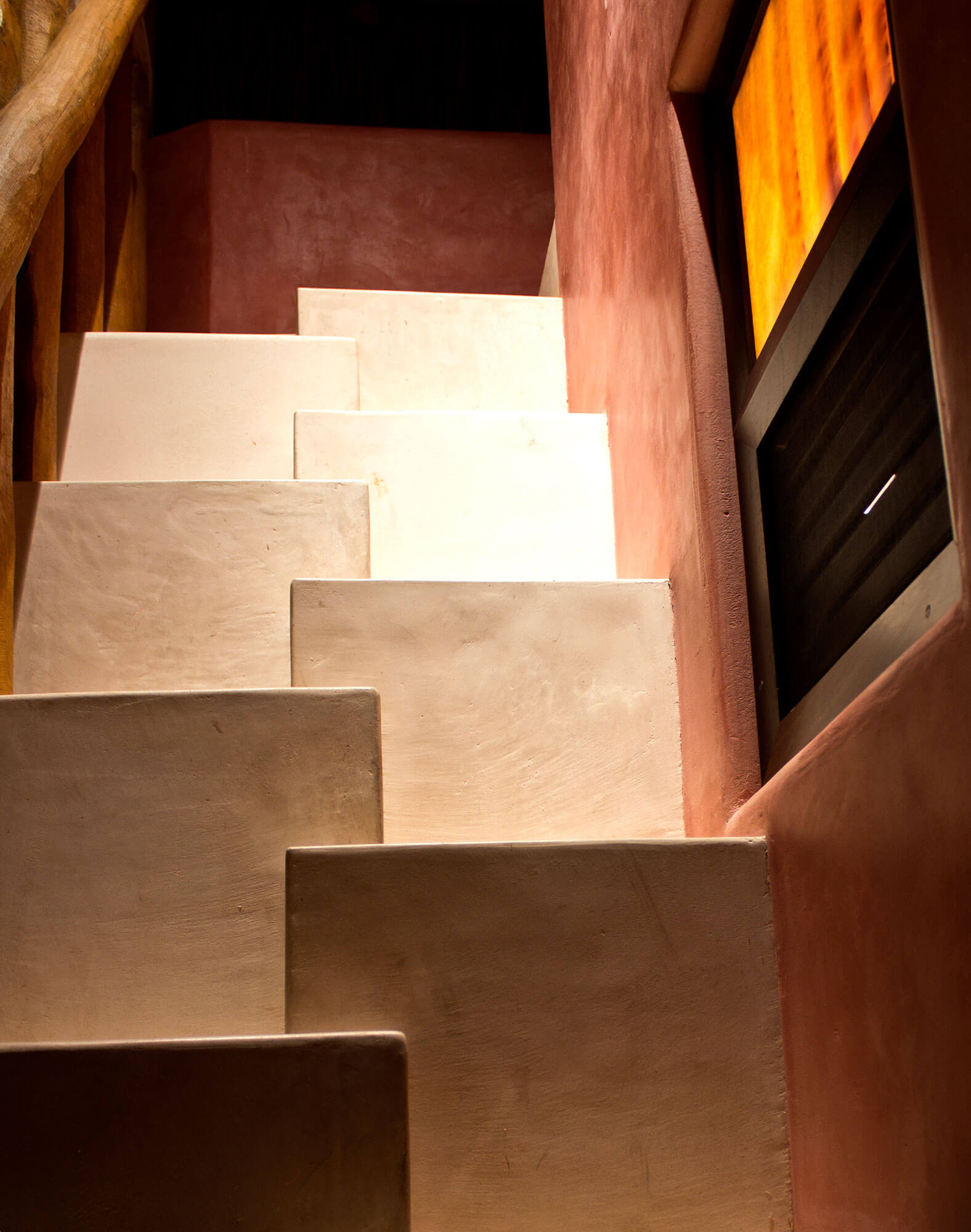 Terracotta-plastered interior staircase with pale stone treads, wood handrail, and a wall-mounted screen beside the steps, Estate Venado, Ranchos Estates, Punta Mita.