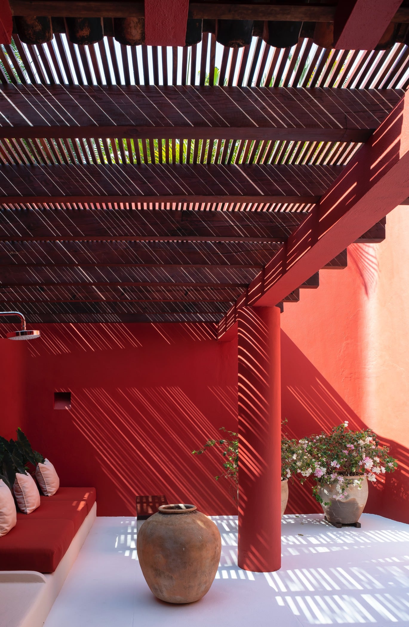 Red-walled outdoor shower courtyard under a slatted wood pergola casting striped shadows, Villa Pacífica, Ranchos Estates, Punta Mita.