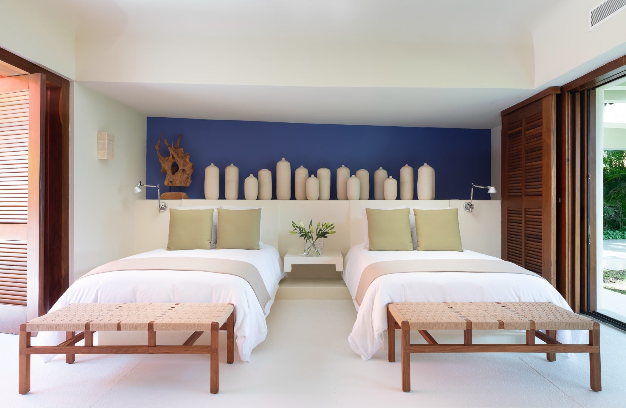 Guest suite with two queen beds, indigo accent wall, and a row of ceramic vessels on a display shelf, Villa Pacífica, Ranchos Estates, Punta Mita.