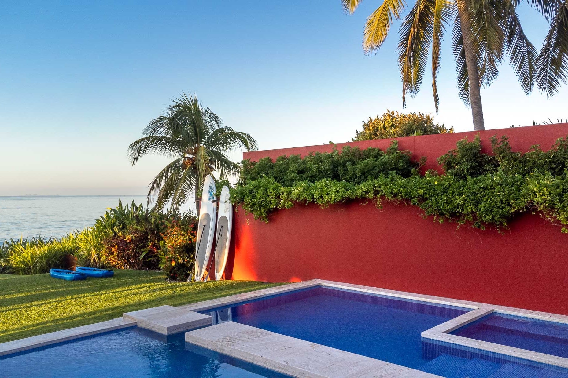 Two stand-up paddleboards leaning on a red garden wall beside the pool, Pacific visible beyond, Villa Pacífica, Ranchos Estates, Punta Mita.