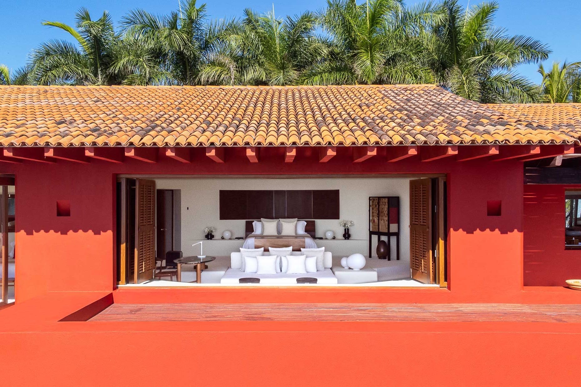 Primary suite viewed from the terrace through open folding doors, showing the walnut headboard and white bedding, Villa Pacífica, Ranchos Estates, Punta Mita.