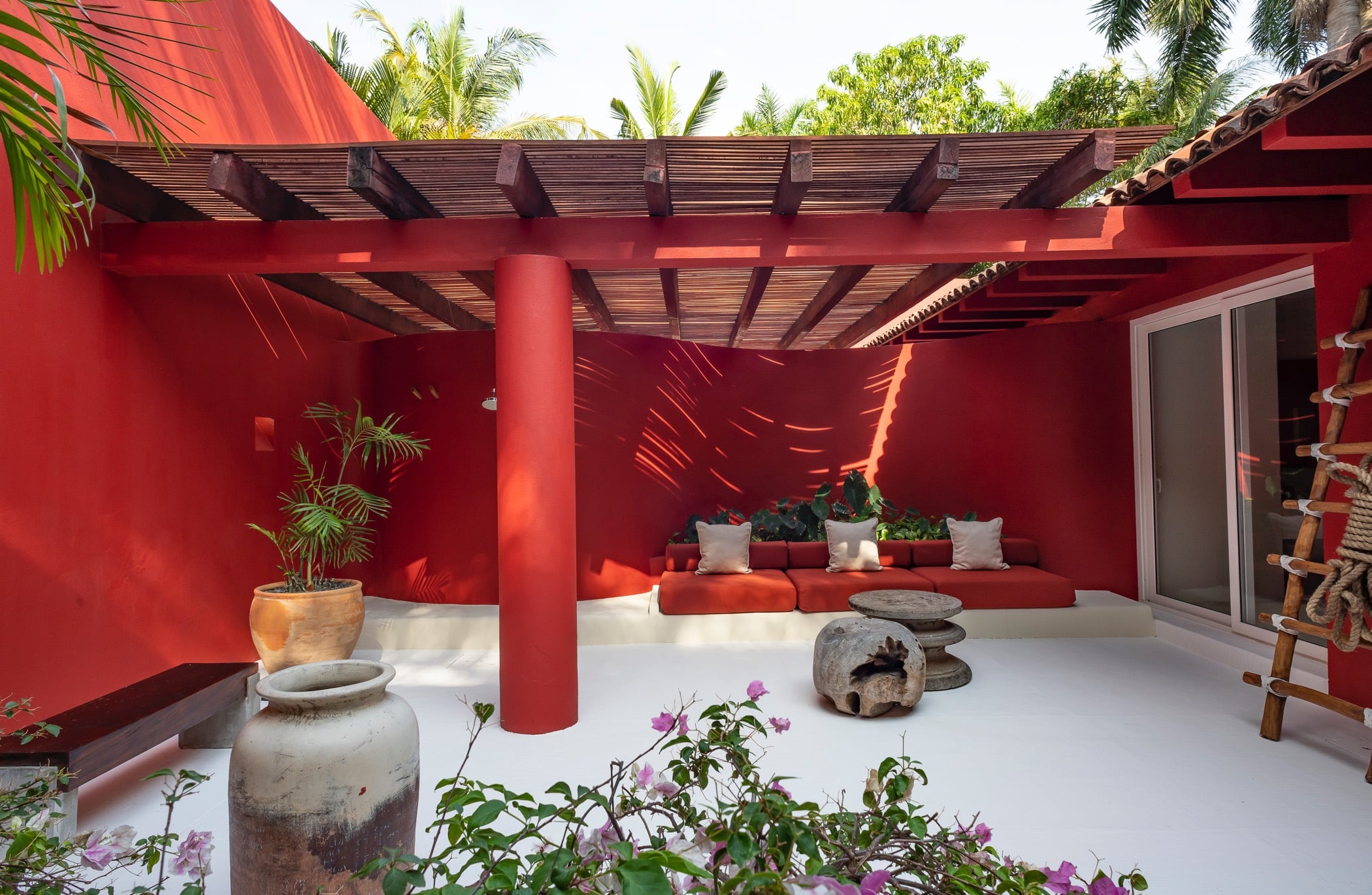 Red-walled terrace with bamboo pergola, built-in lounge seating, and bougainvillea in the foreground, Villa Pacífica, Ranchos Estates, Punta Mita.