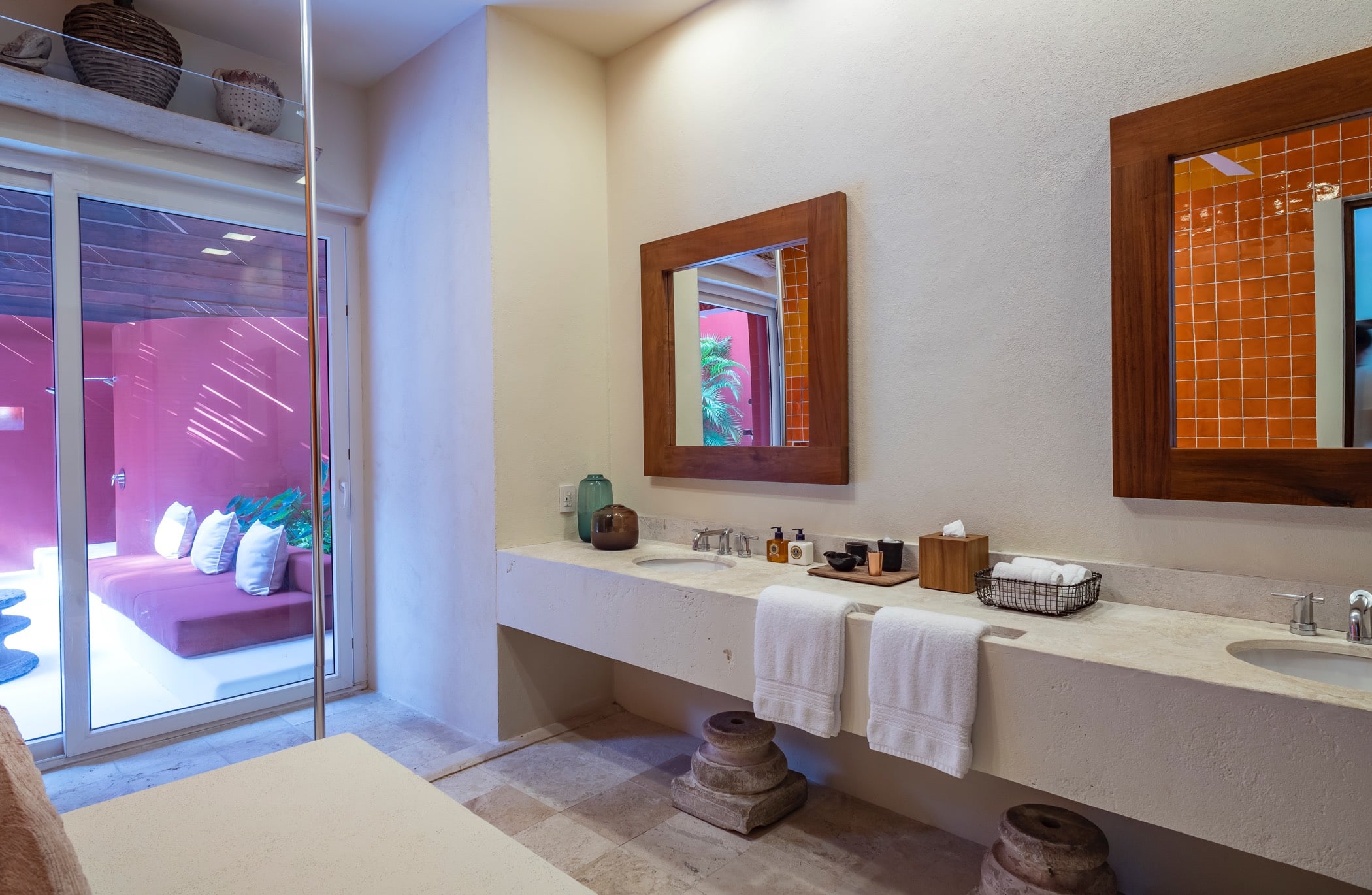 Double-vanity ensuite bathroom with teak-framed mirrors, orange tile accents, and a glass door opening to a purple-walled bedroom, Villa Pacífica, Ranchos Estates, Punta Mita.