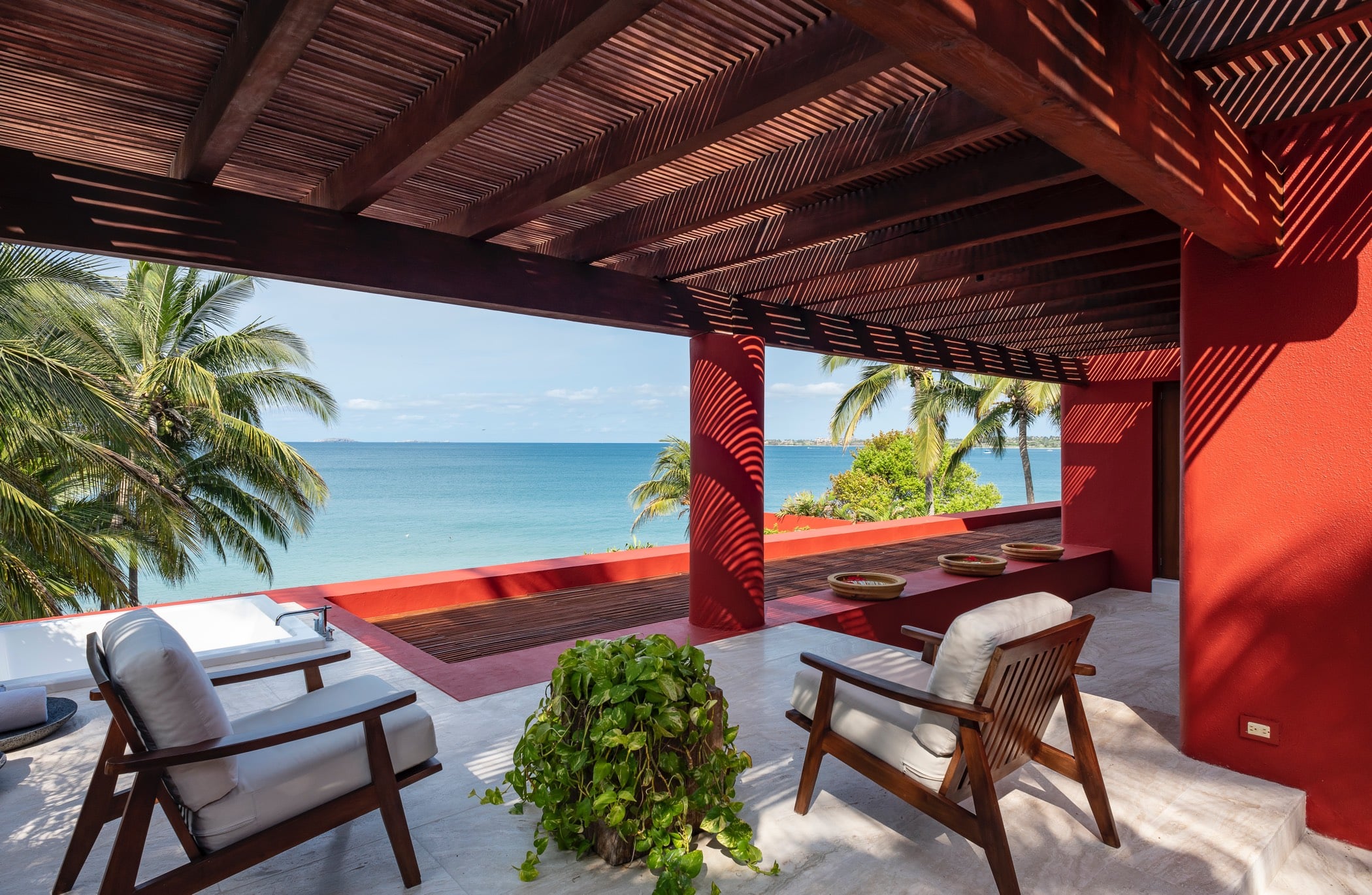 Upper terrace with two teak armchairs beneath a slatted wood pergola, red columns, potted vine, and a broad view of the Pacific Ocean, Villa Pacífica, Ranchos Estates, Punta Mita.