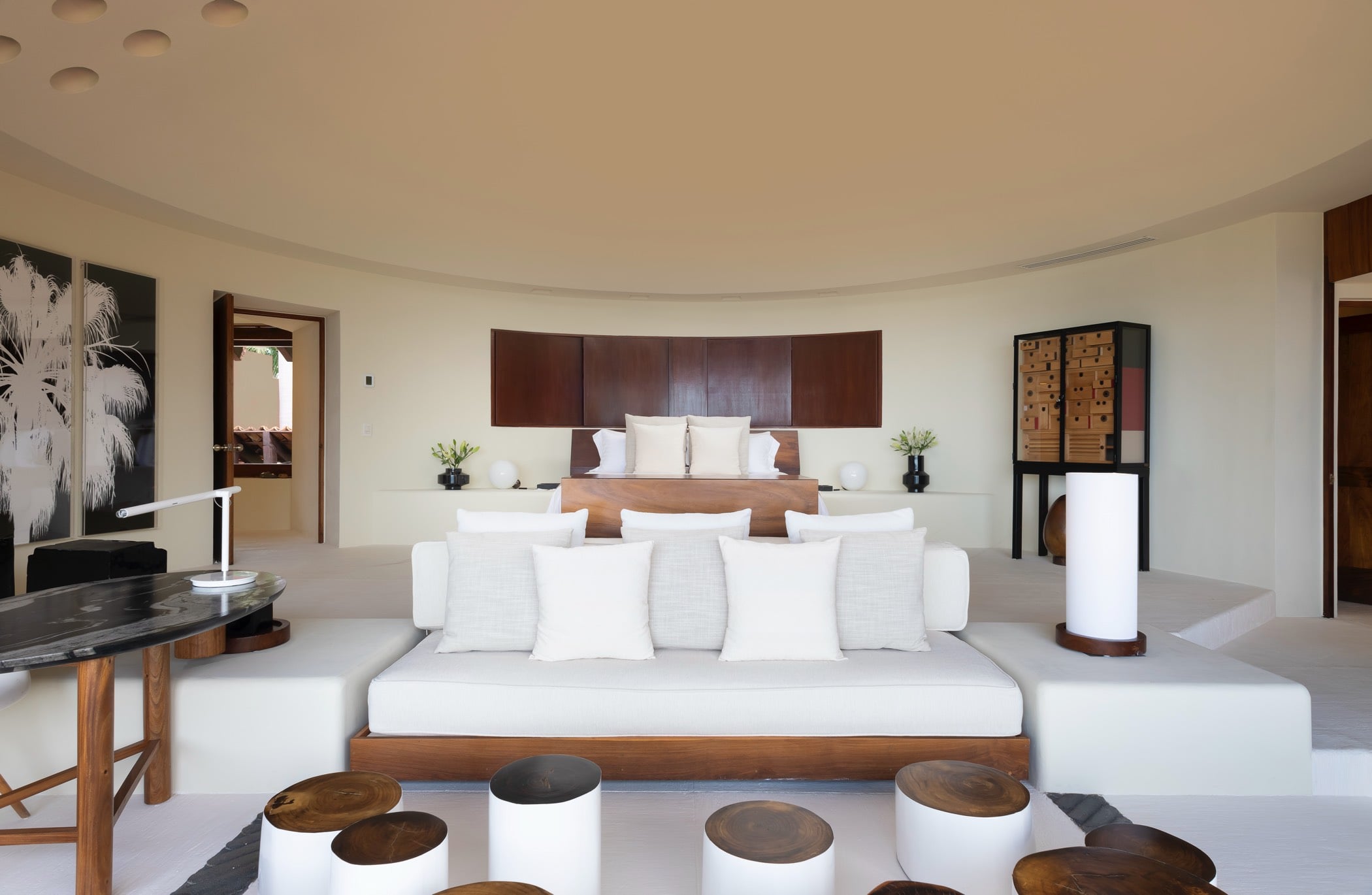 Curved-ceiling primary suite with king bed, dark wood headboard, white daybed bench, marble desk, and sculptural cabinet, Villa Pacífica, Ranchos Estates, Punta Mita.