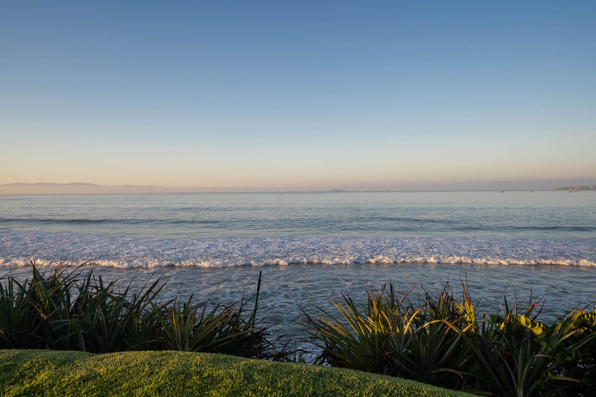 Pacific Ocean view at dawn from the villa's beachfront lawn, gentle surf breaking, distant Marietas Islands silhouette on the horizon, low coastal plantings in foreground, Villa Pacífica, Ranchos Estates, Punta Mita.