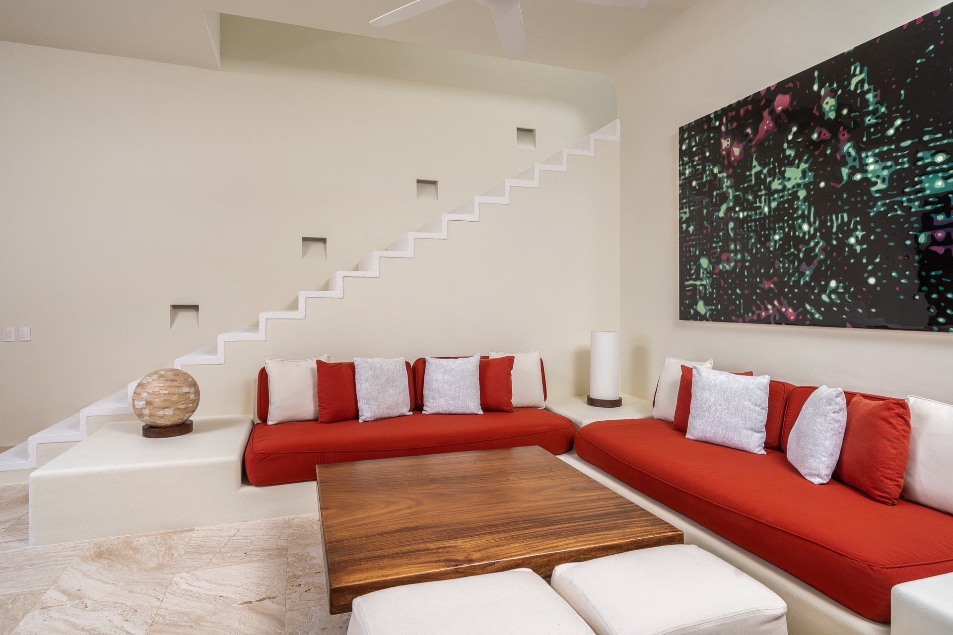 Low red sectional sofas around a walnut coffee table below a sculptural staircase, large abstract canvas on the wall, Villa Pacífica, Ranchos Estates, Punta Mita.