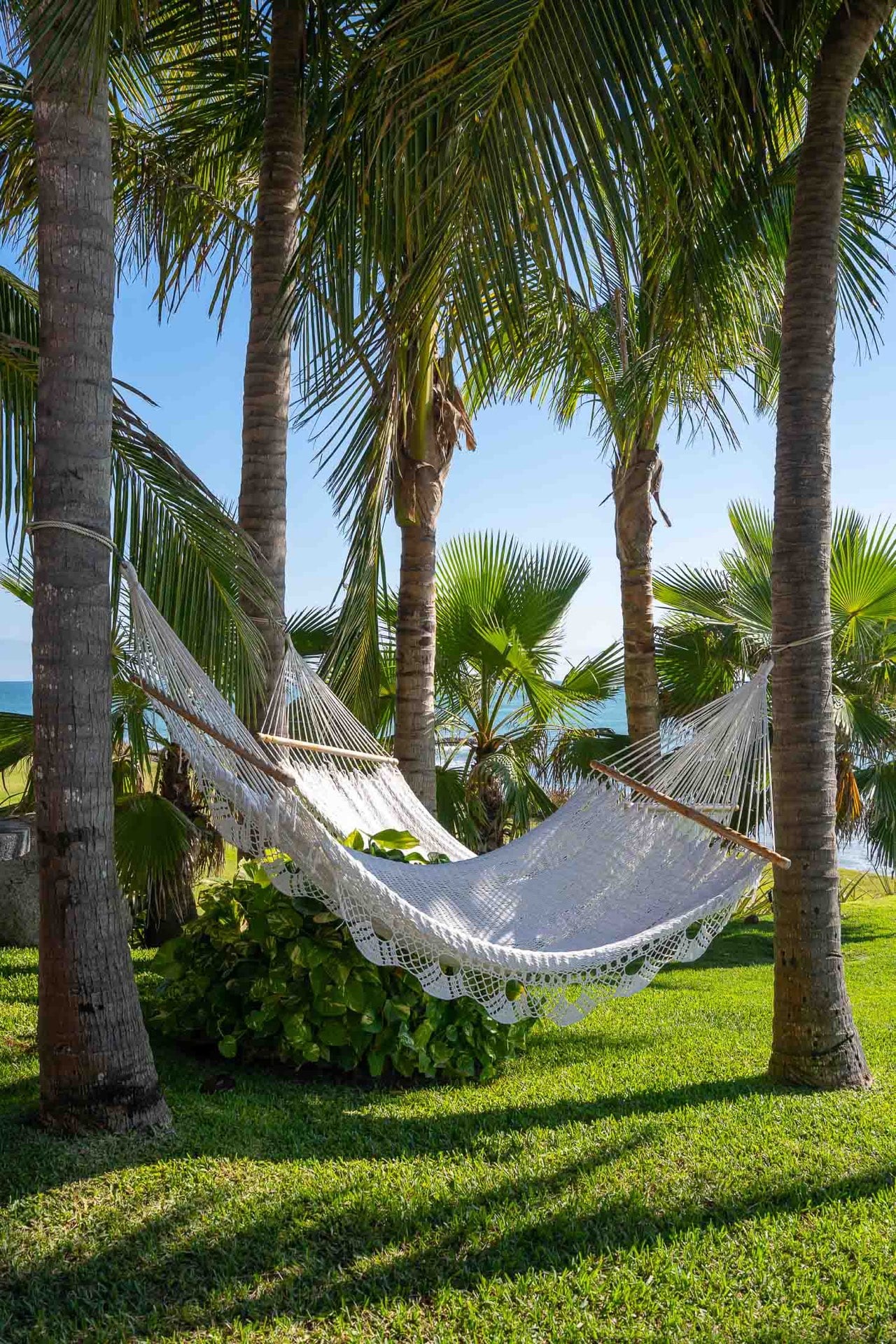 Woven cotton hammock strung between two coconut palms on the garden lawn, a glimpse of the ocean beyond, Villa Pacífica, Ranchos Estates, Punta Mita.