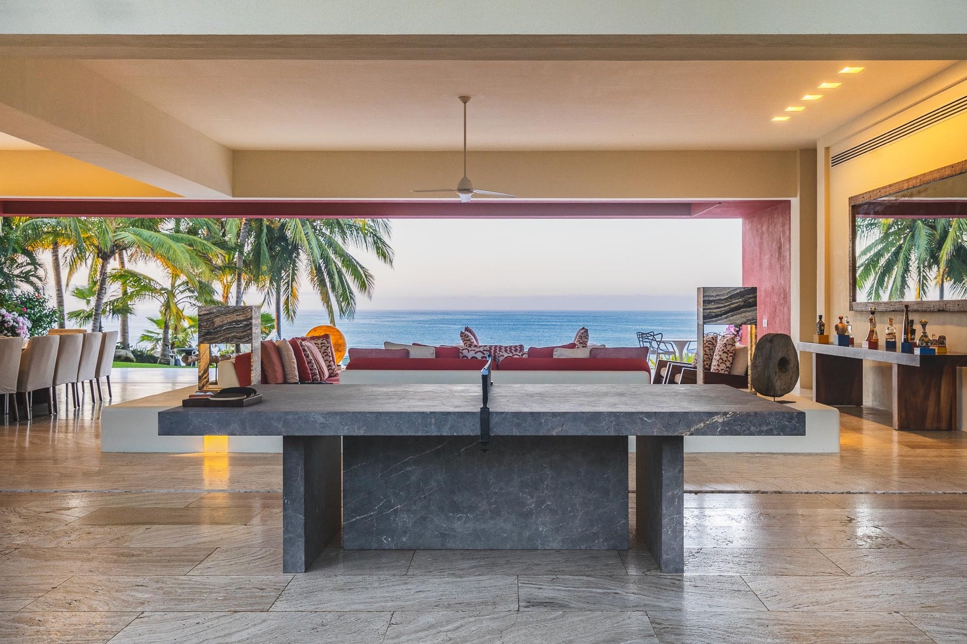 A full-size ping-pong table in dark slate stone occupies the center of the media room, which opens directly to the living pavilion and a palm-framed ocean horizon, Villa Pacífica, Ranchos Estates, Punta Mita.