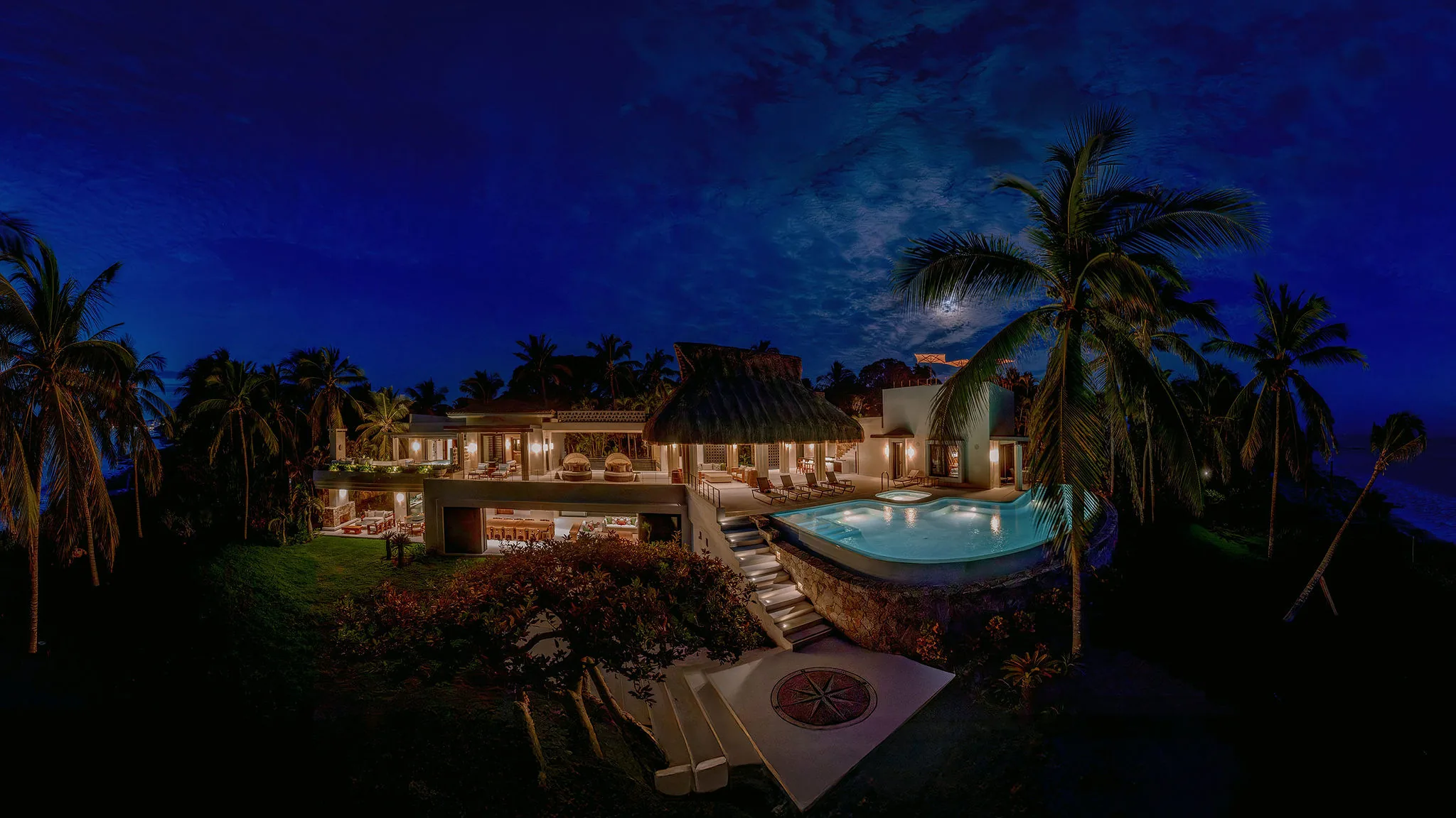 Casa Happy Paws, a luxury Punta Mita villa in Ranchos Estates, boasts big windows, pool, palms, and tropical plants at night.
