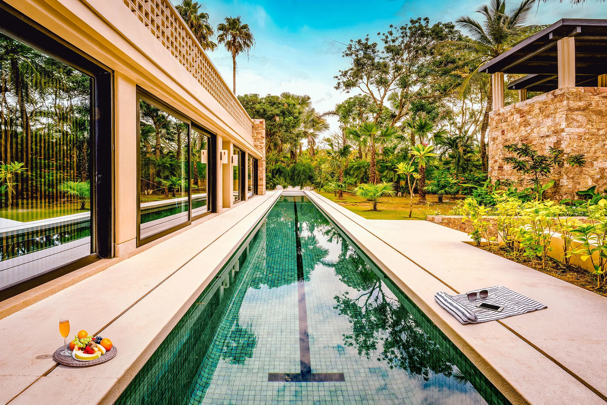 Long narrow pool by Casa Happy Paws, a modern Punta Mita Ranchos Estates home with lush greenery and poolside refreshments.