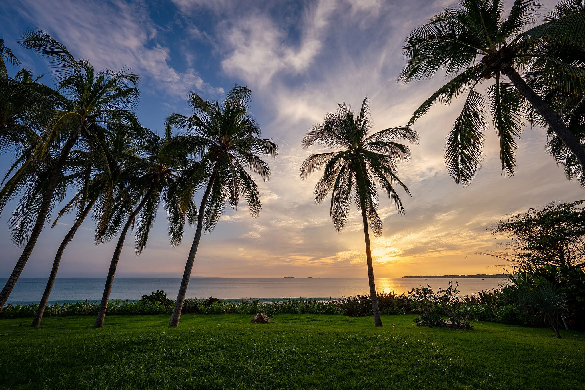 Sunset ocean view at Casa Happy Paws, Punta Mita's Ranchos Estates: palm trees, lawn, vibrant sky, calm sea.