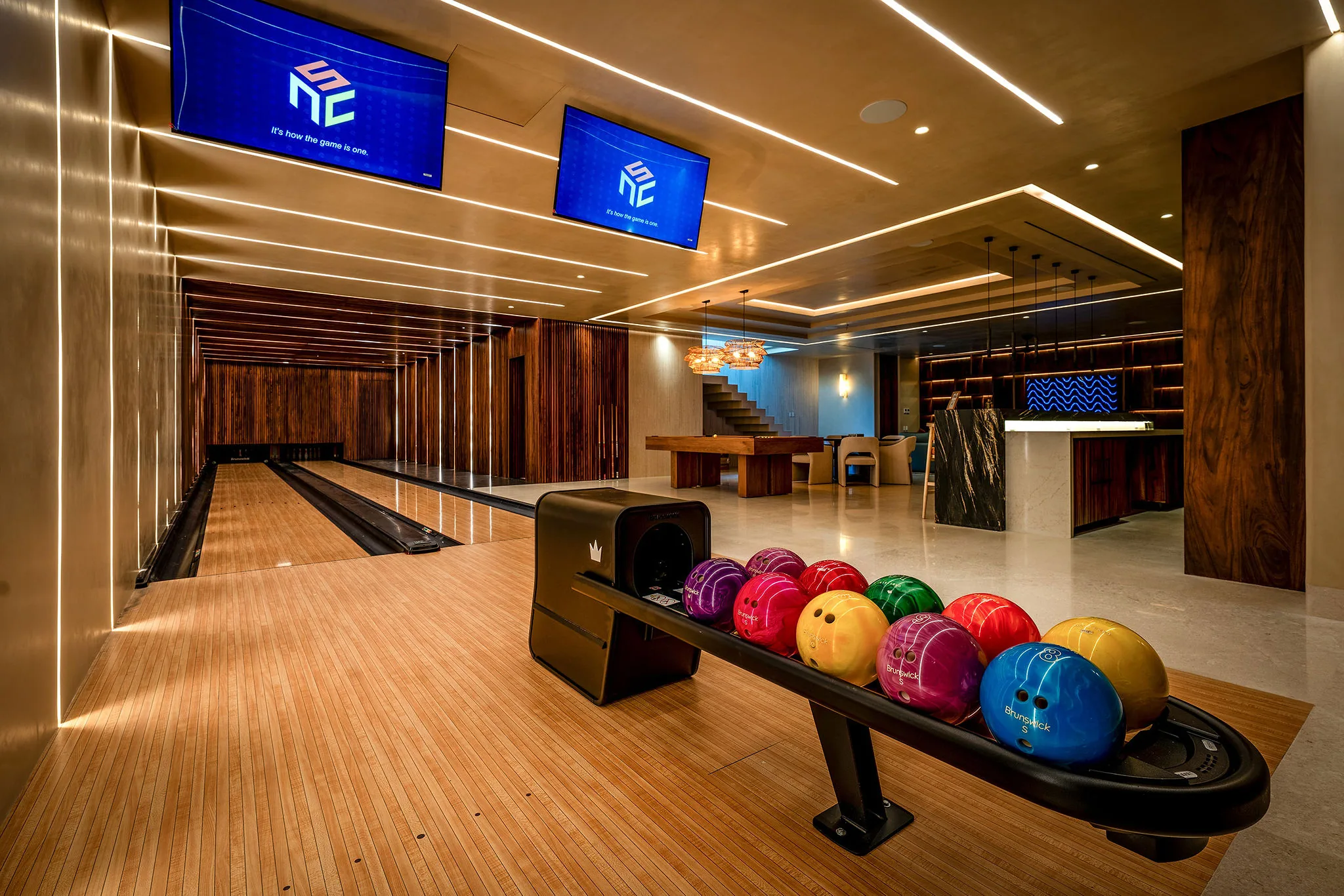 Modern Punta Mita bowling alley with two lanes, wood floors, vibrant balls, big screens, bar seating—ideal for Ranchos Estates fun.