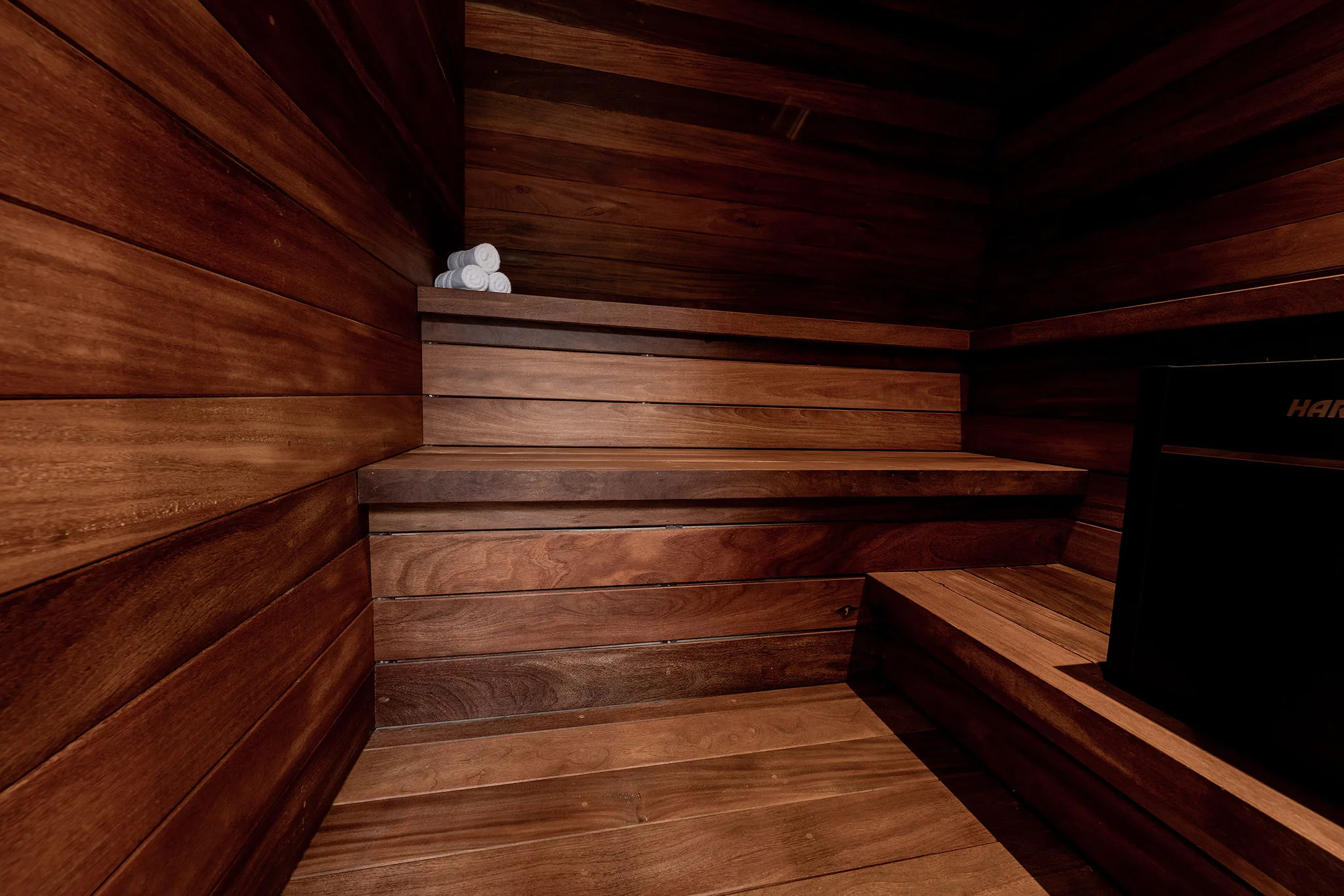 Modern wooden sauna in Casa Happy Paws, Punta Mita, with tiered benches, dark wood panels, towels, and black heater.