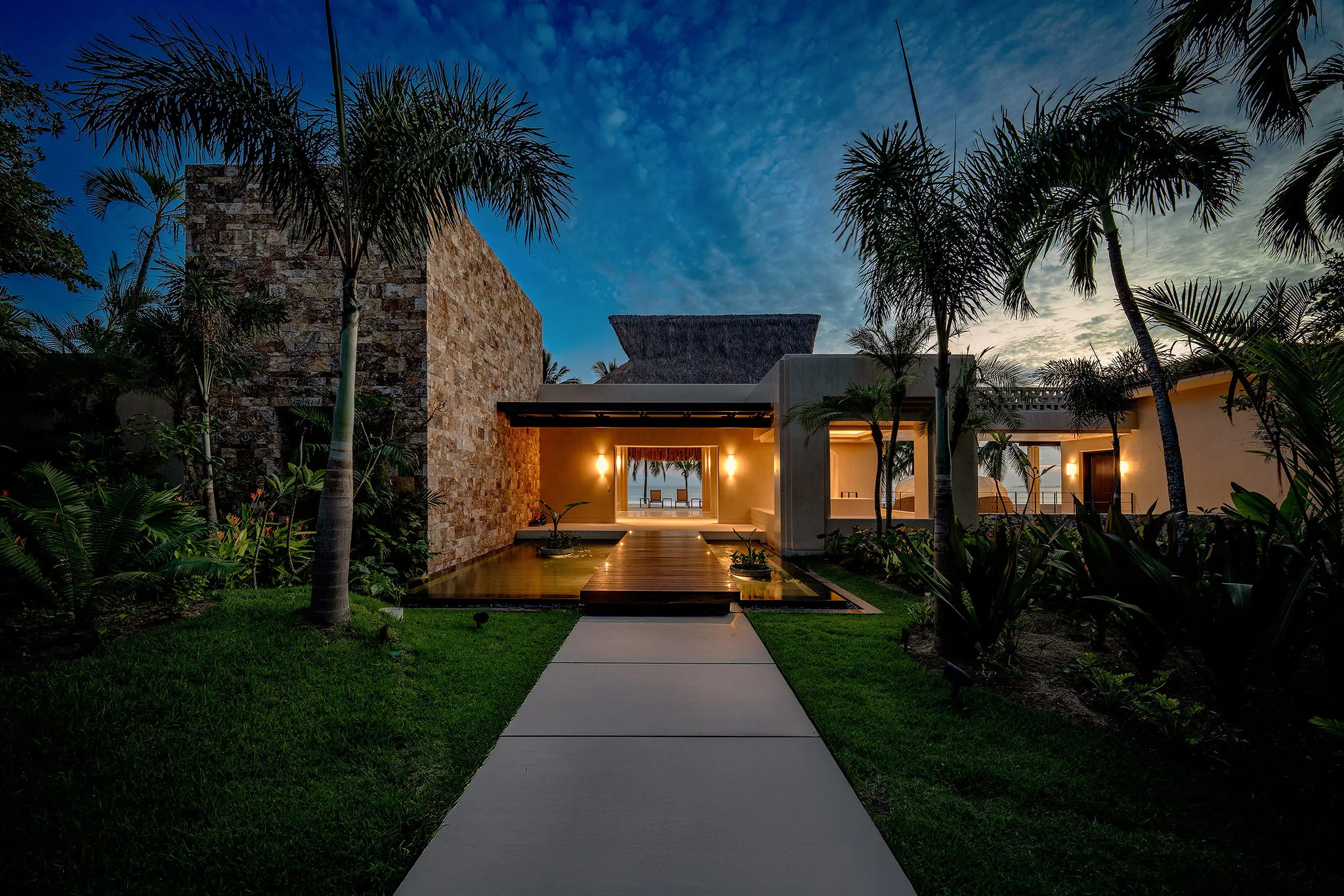 Casa Happy Paws in Ranchos Estates, Punta Mita: modern stone-and-stucco home with large windows, palms, and dusk lighting.