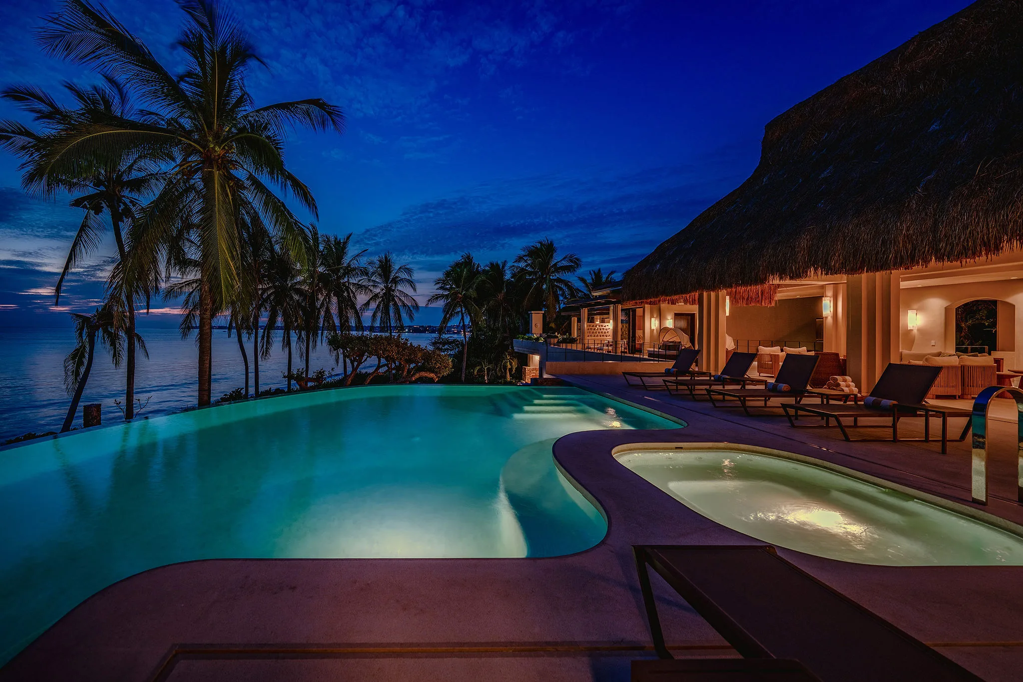 Infinity pool and jacuzzi at Casa Happy Paws, Ranchos Estates, Punta Mita, overlook ocean sunset framed by palms and loungers.