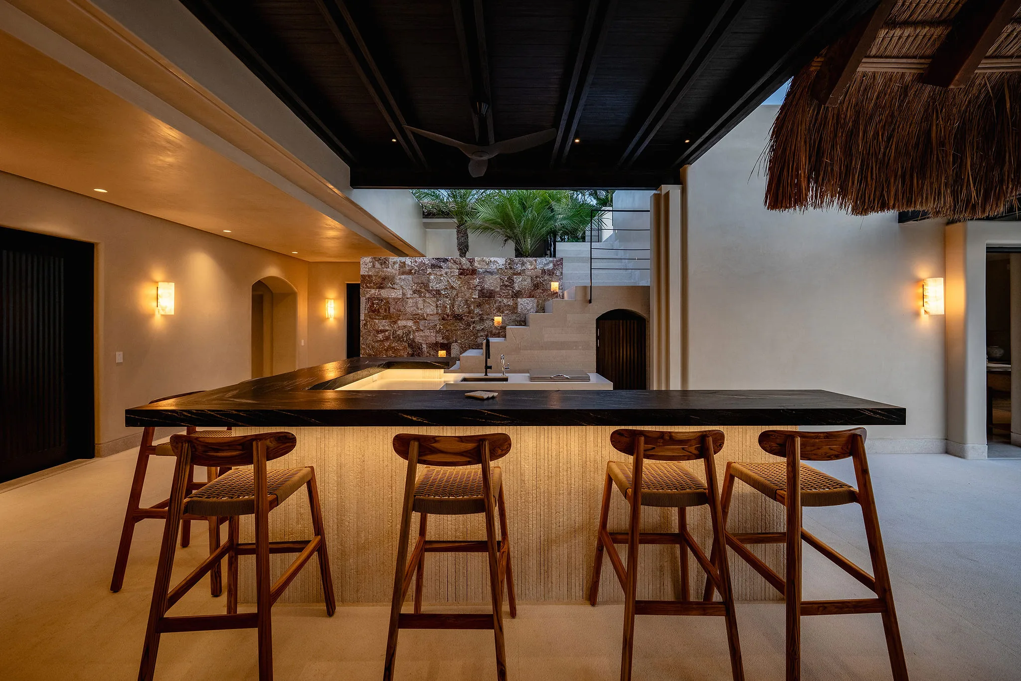 Casa Happy Paws: sleek outdoor kitchen in Punta Mita’s Ranchos Estates with island, bar stools, tropical plants, open ceiling.